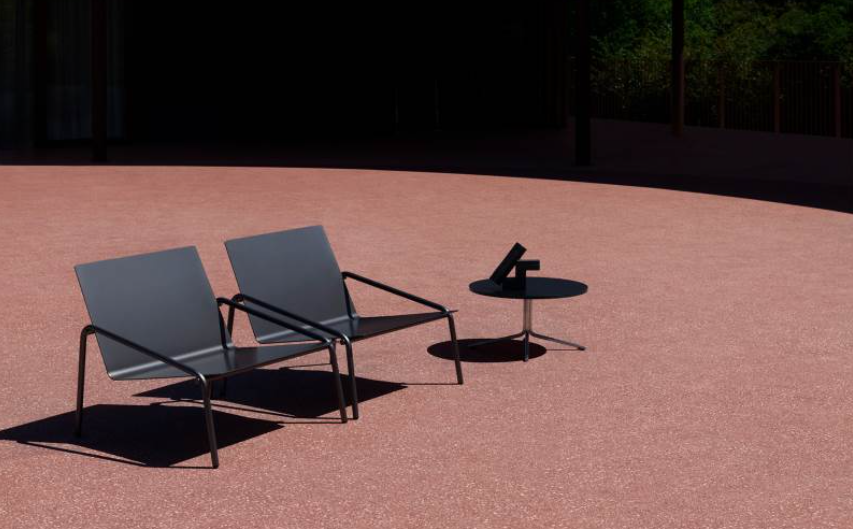 Empty outdoor seating area with two metal chairs and a small table on a reddish-brown surface.