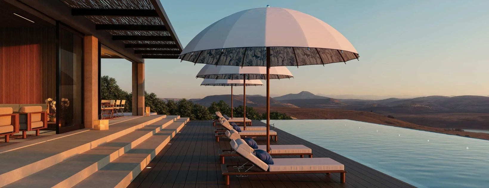 Outdoor terrace with lounge chairs and umbrellas overlooking a landscape at sunset.