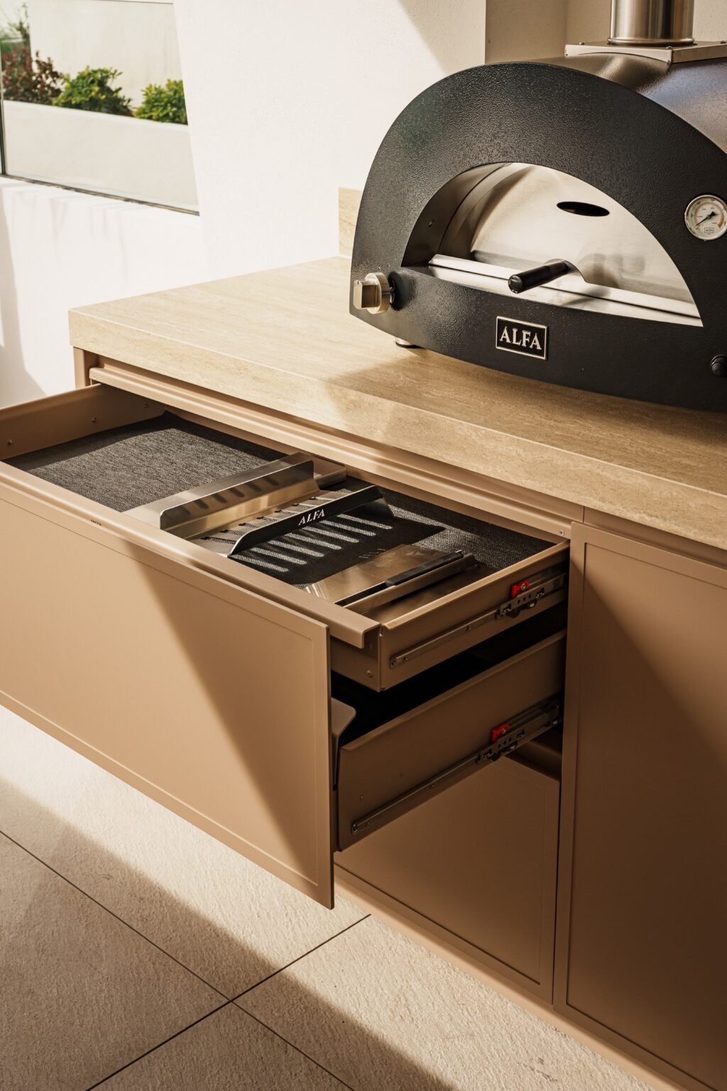 Close-up of a pasta machine on a kitchen counter and a drawer with a metallic food slicer inside.