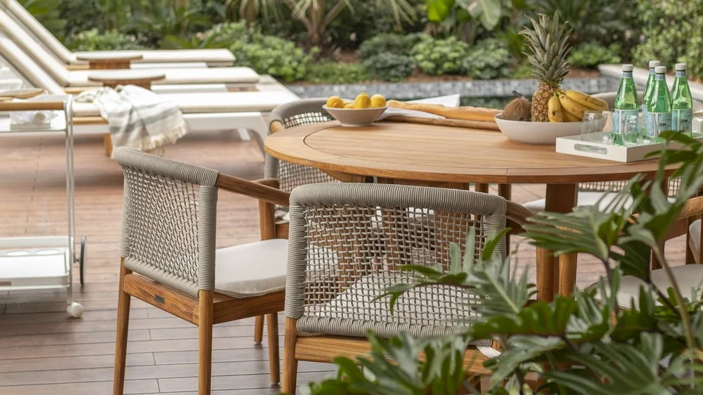 Outdoor patio with wooden table, chairs, and lounge chairs, decorated with fruit and bottled water.
