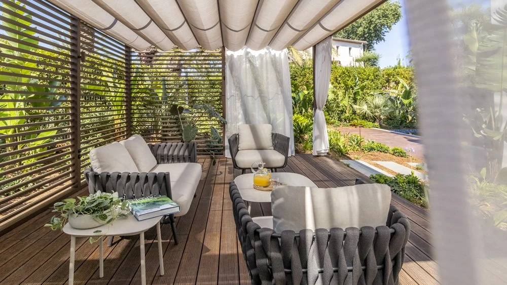 Outdoor patio with wooden flooring, cushioned seating, and lush green garden surroundings.