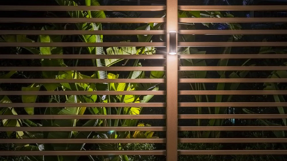 View through horizontal wooden slats revealing green tropical plants with variegated leaves behind.