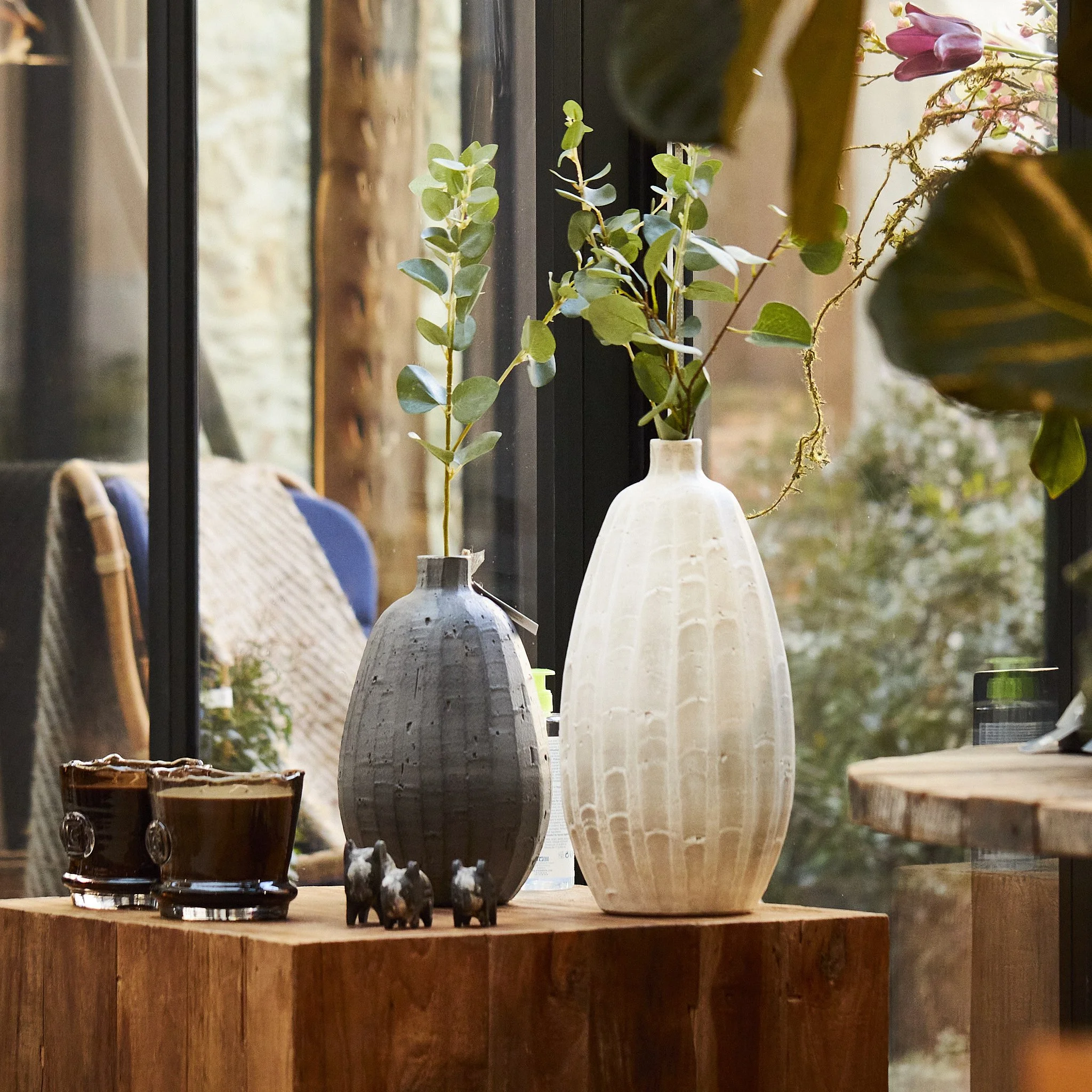 Display of various ceramic vases and containers with plants inside, placed on a wooden surface.