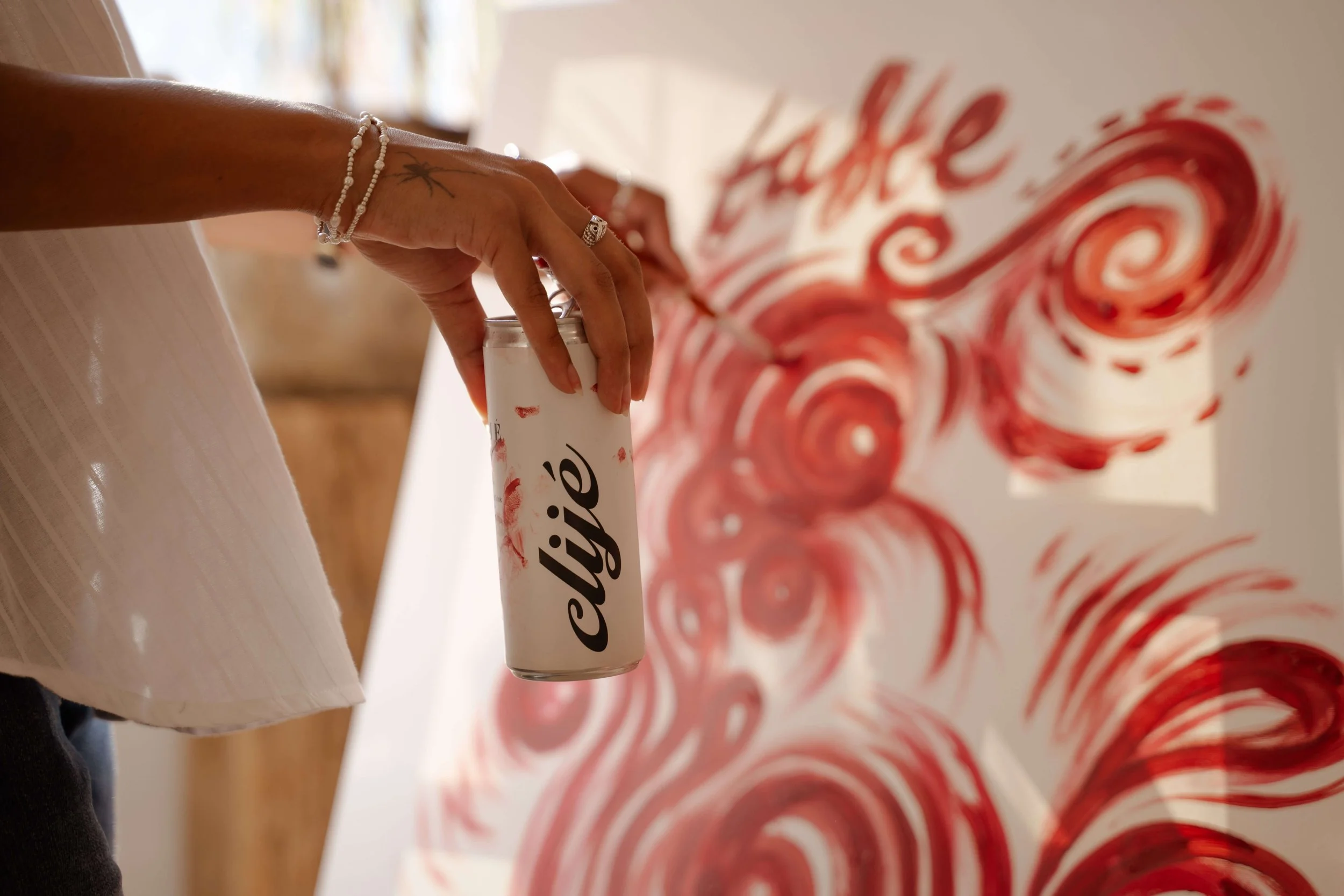A person's hand holding a white can of Coca-Cola with a red swirl pattern in the background.