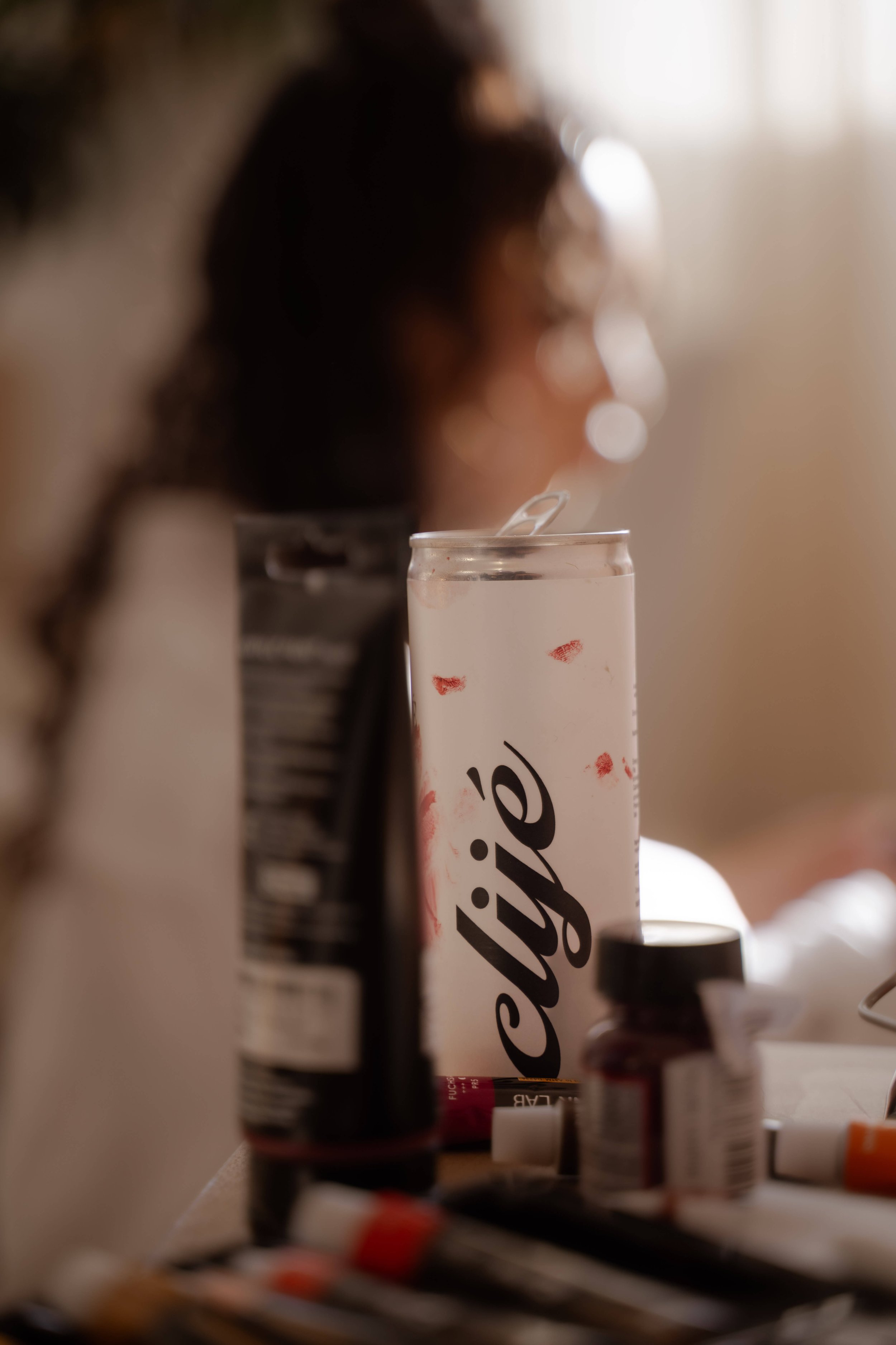 A blurred image of a woman with dark hair in the background focusing on a clipboard or container with the word 'safety' visible on it, surrounded by various medicine bottles and items on a surface.