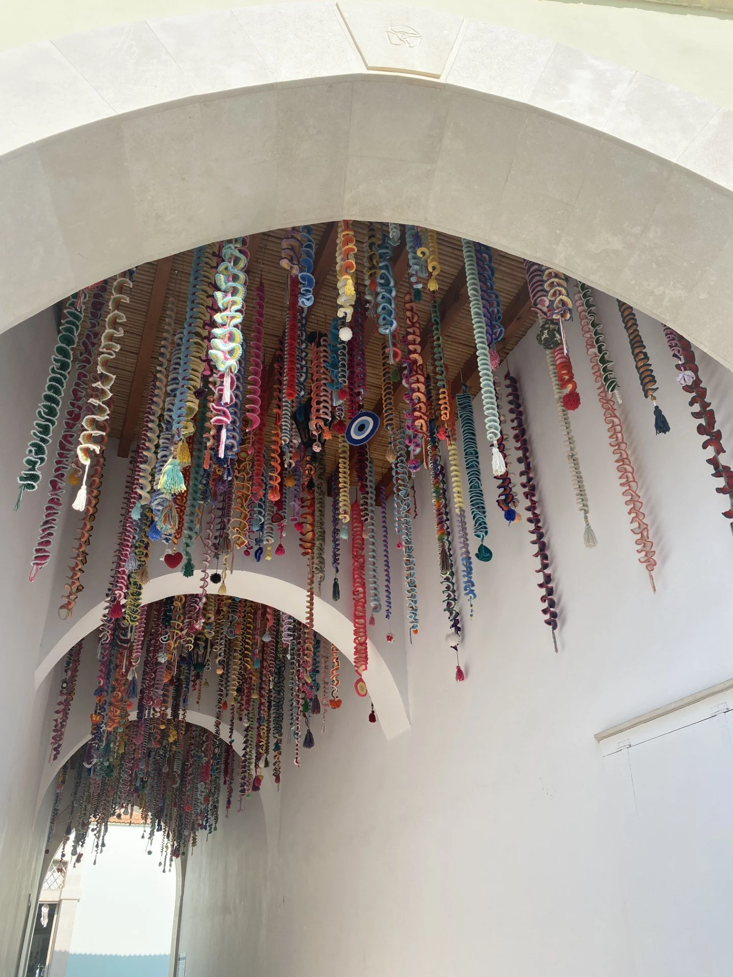 Colourful crocheted dangly decorations hang from the ceiling of a smooth white archway in Cyprus.