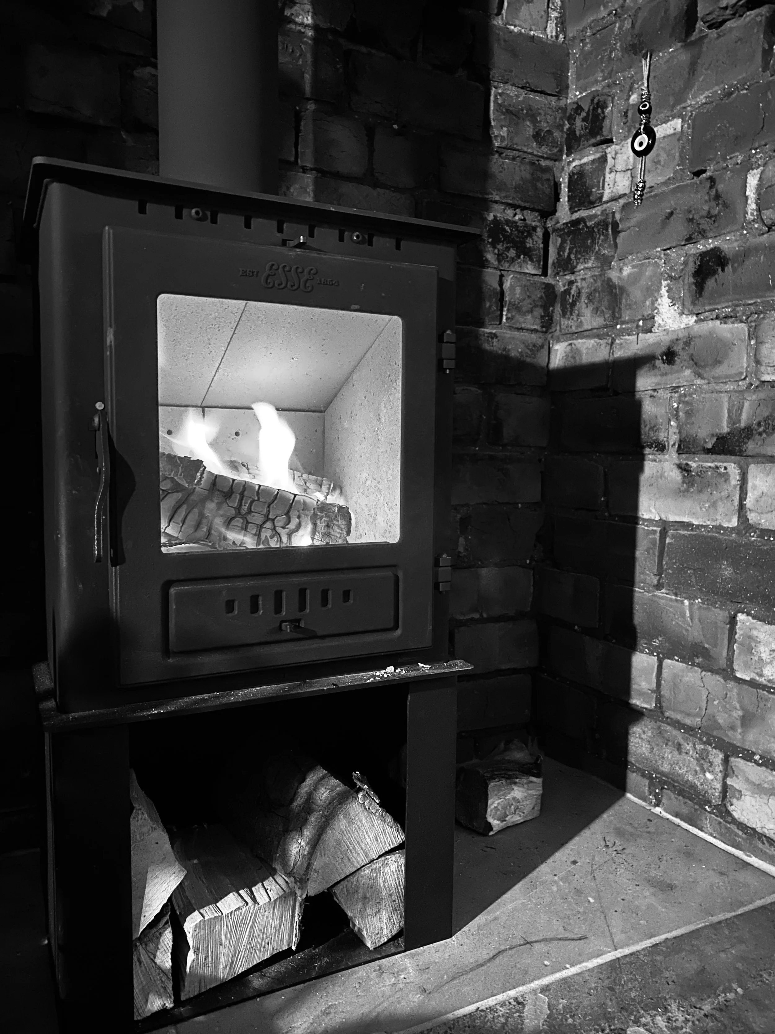 Black and white image of a fire inside a black log burner. The exposed bricks of the fireplace can be seen in the background.