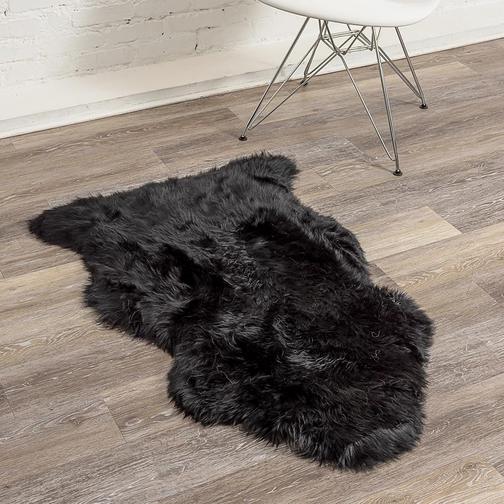 A black fur rug on a wooden floor next to a white chair with metal legs in a room with white brick walls.