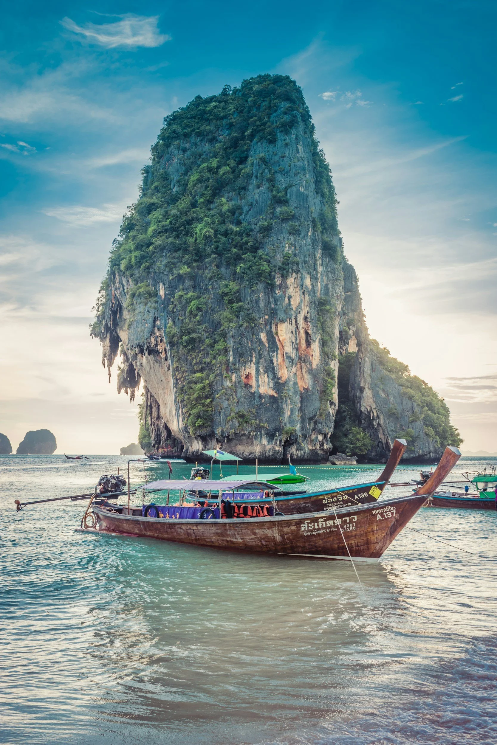 Longtail boat floating in the sea with a large limestone cliff covered in green vegetation in the background.
