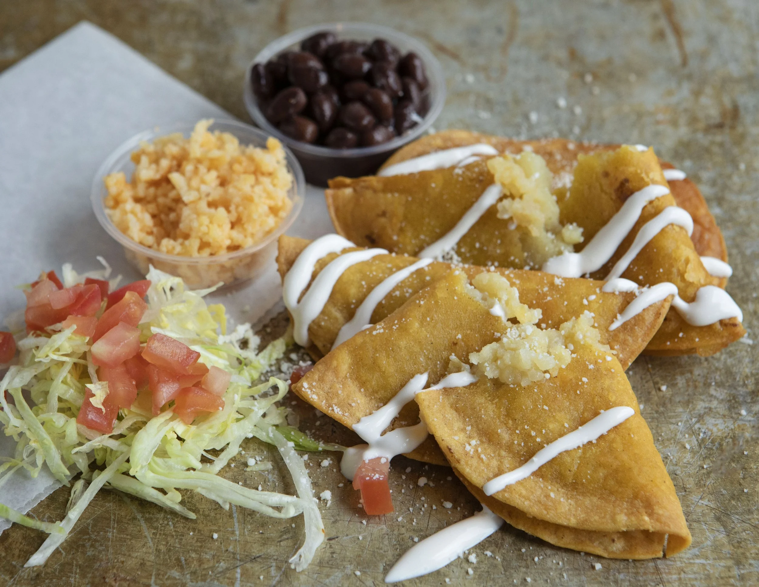 Mashed potatoes filled  taquitos topped with sour cream, served with black beans, shredded cheese, and a side of chopped lettuce and tomatoes.