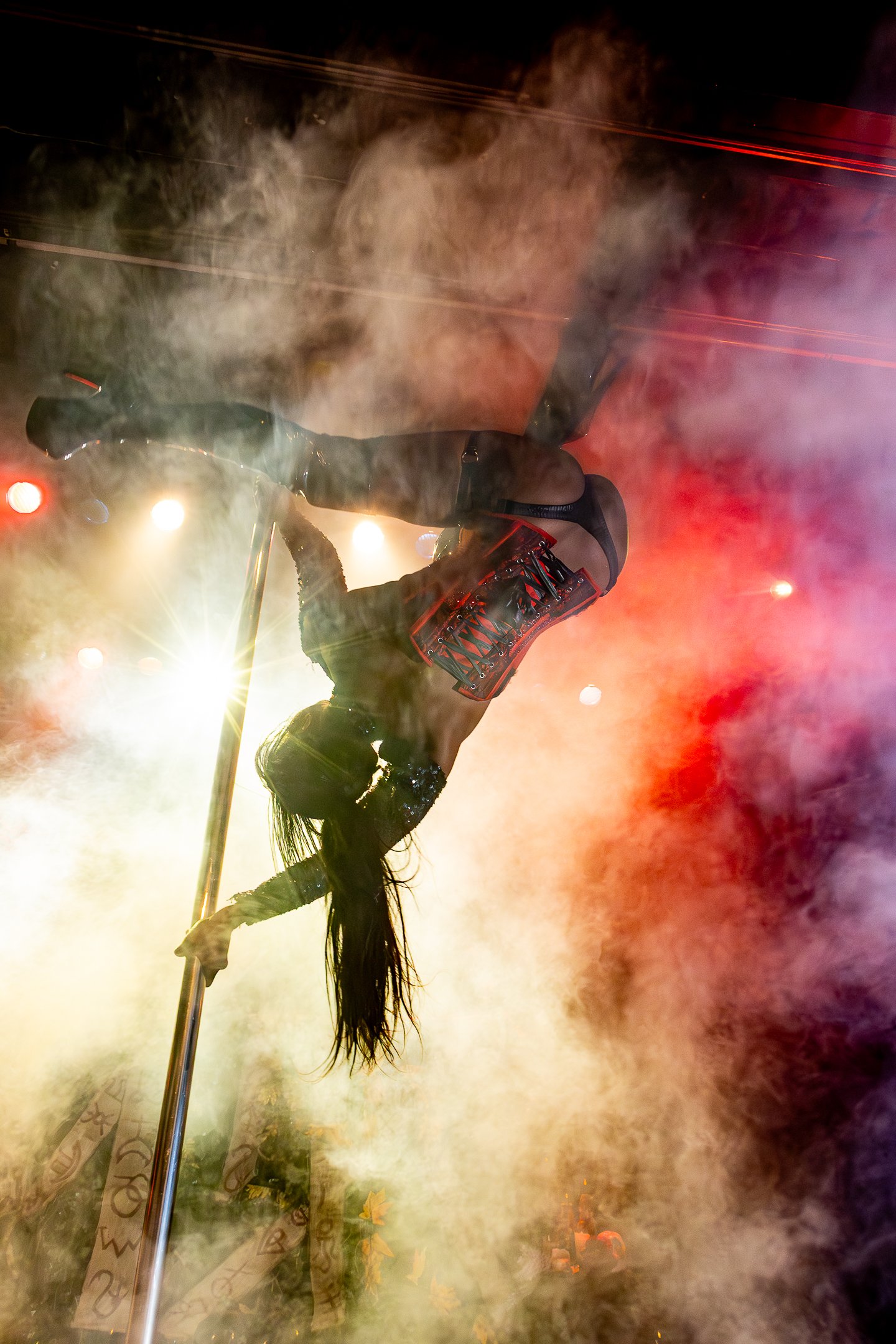 A performer on stilts holding a flag, surrounded by smoke and colorful stage lights.