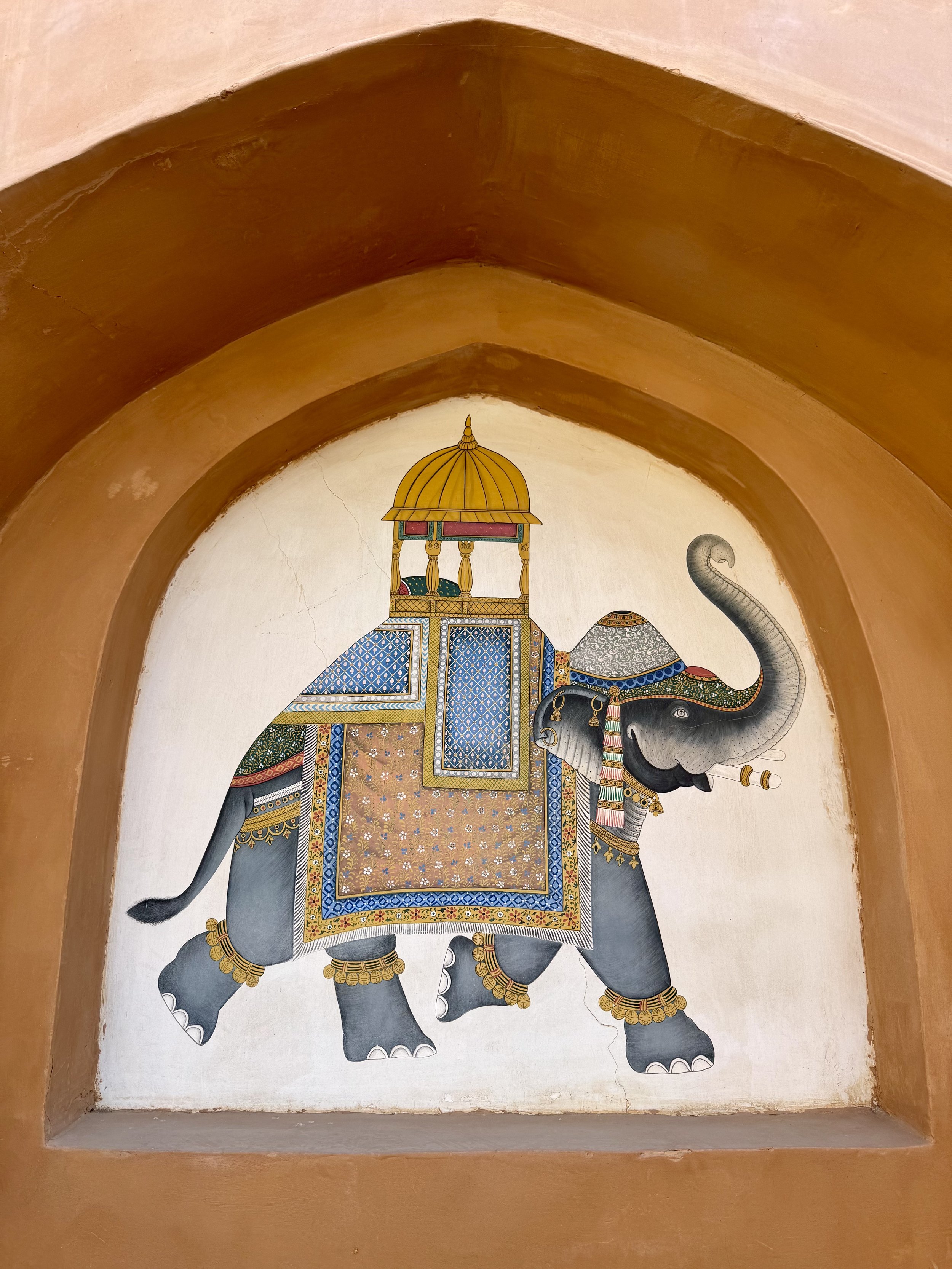 Decorative painting of an ornate gray elephant with colorful patterns, topped with a golden canopy, inside a decorative arch.