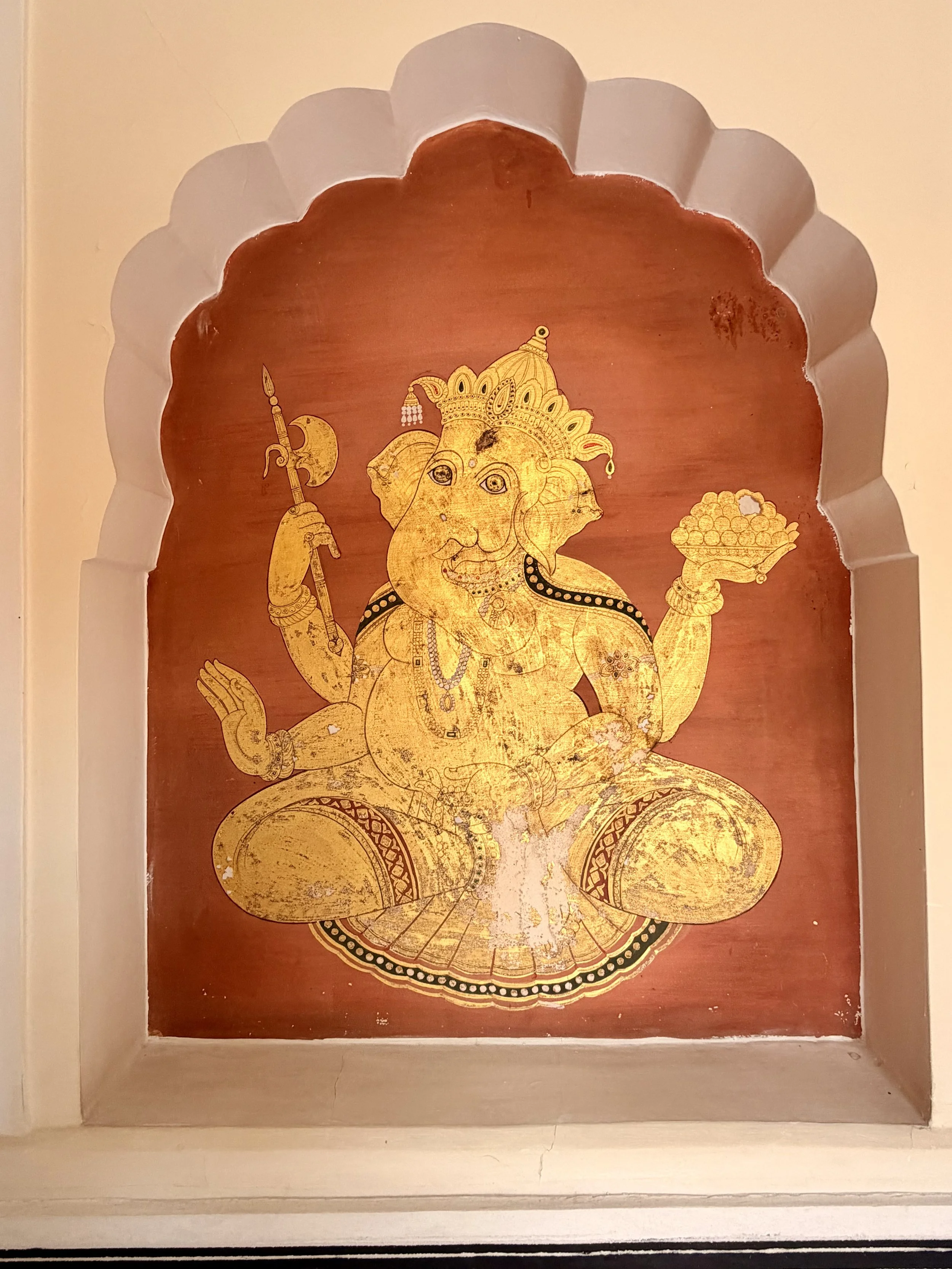 Gold-colored Hindu deity Ganesha painting on a wall with an ornate arched frame.