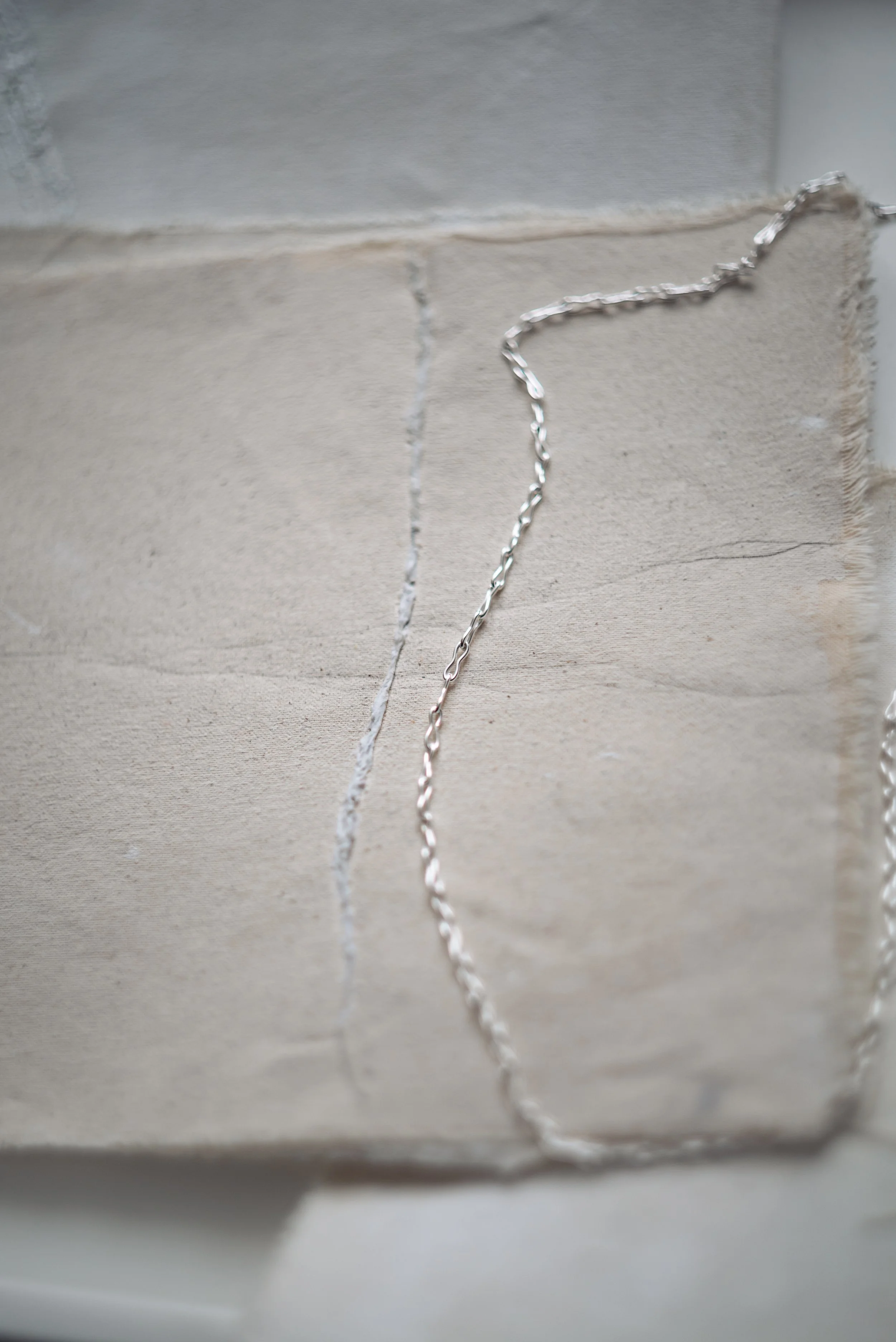 Close-up image of two thin, silver chains hanging on a gradient background of gray and beige tiles.