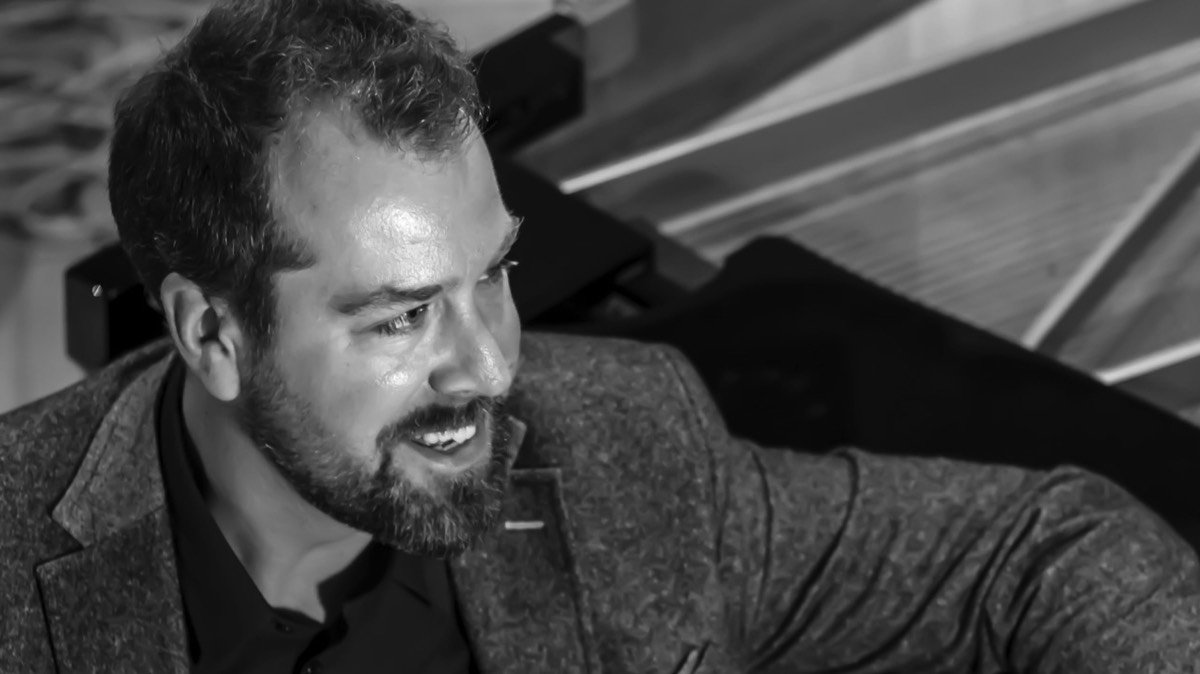 A man with a beard and curly hair playing a piano, captured from an overhead angle in black and white.