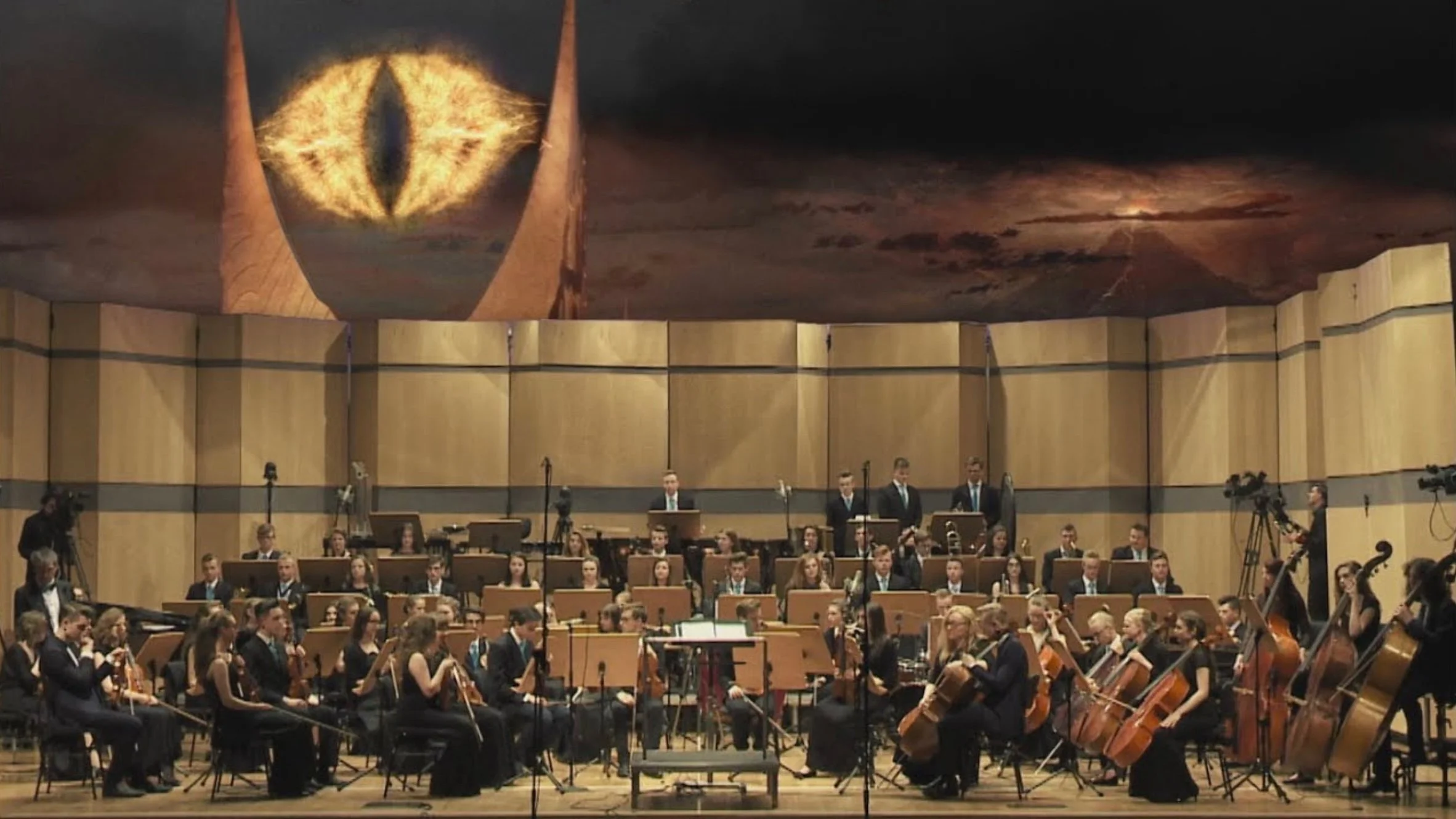 An orchestra performing on stage with musicians playing string, woodwind, and brass instruments, under a large curved ceiling with a painted mural and symmetrical wooden panels.
