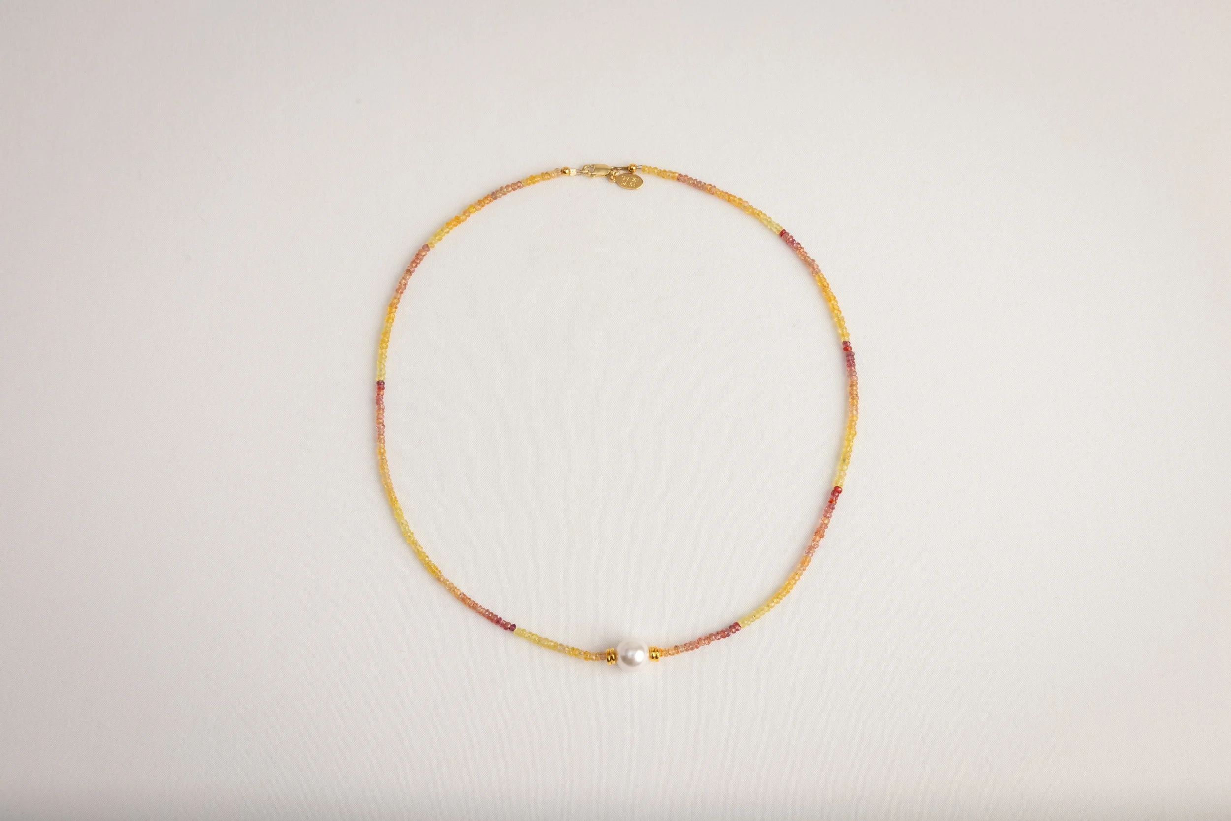 A delicate beaded necklace with a central pearl and gold accents, arranged on a plain white background.