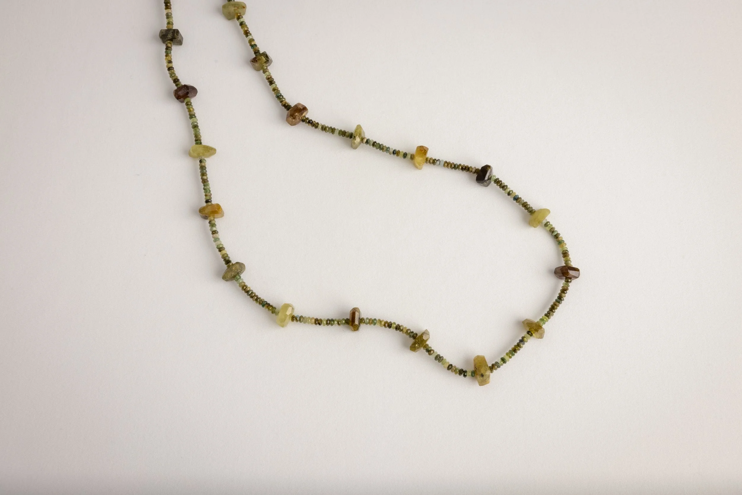 Beaded necklace with various colored and shaped stones, laid on a white background.