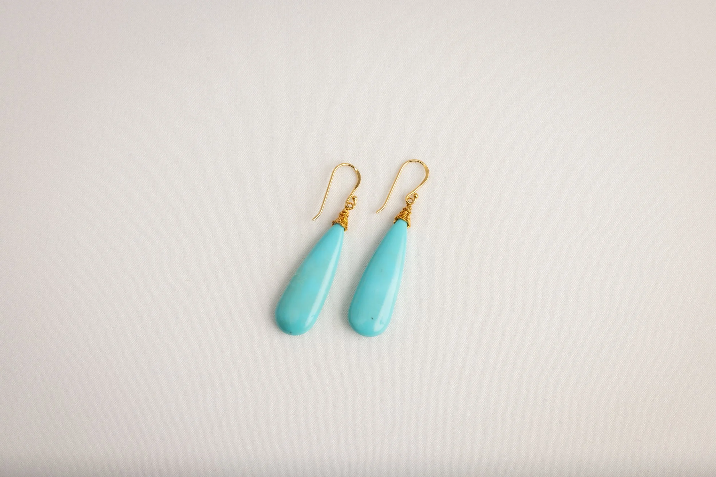 Pair of gold earrings with turquoise teardrop-shaped pendants on a plain white background.