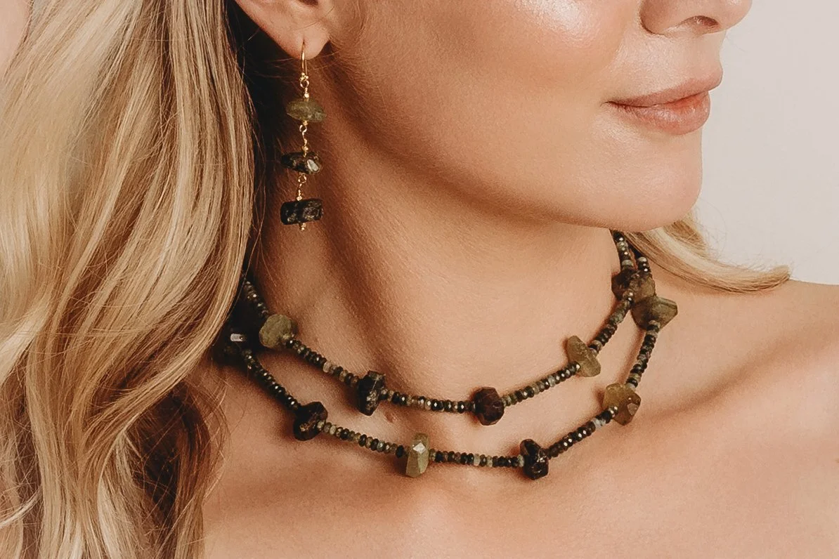 Close-up of a woman wearing layered beaded necklaces and a dangling earring with irregularly shaped beads.