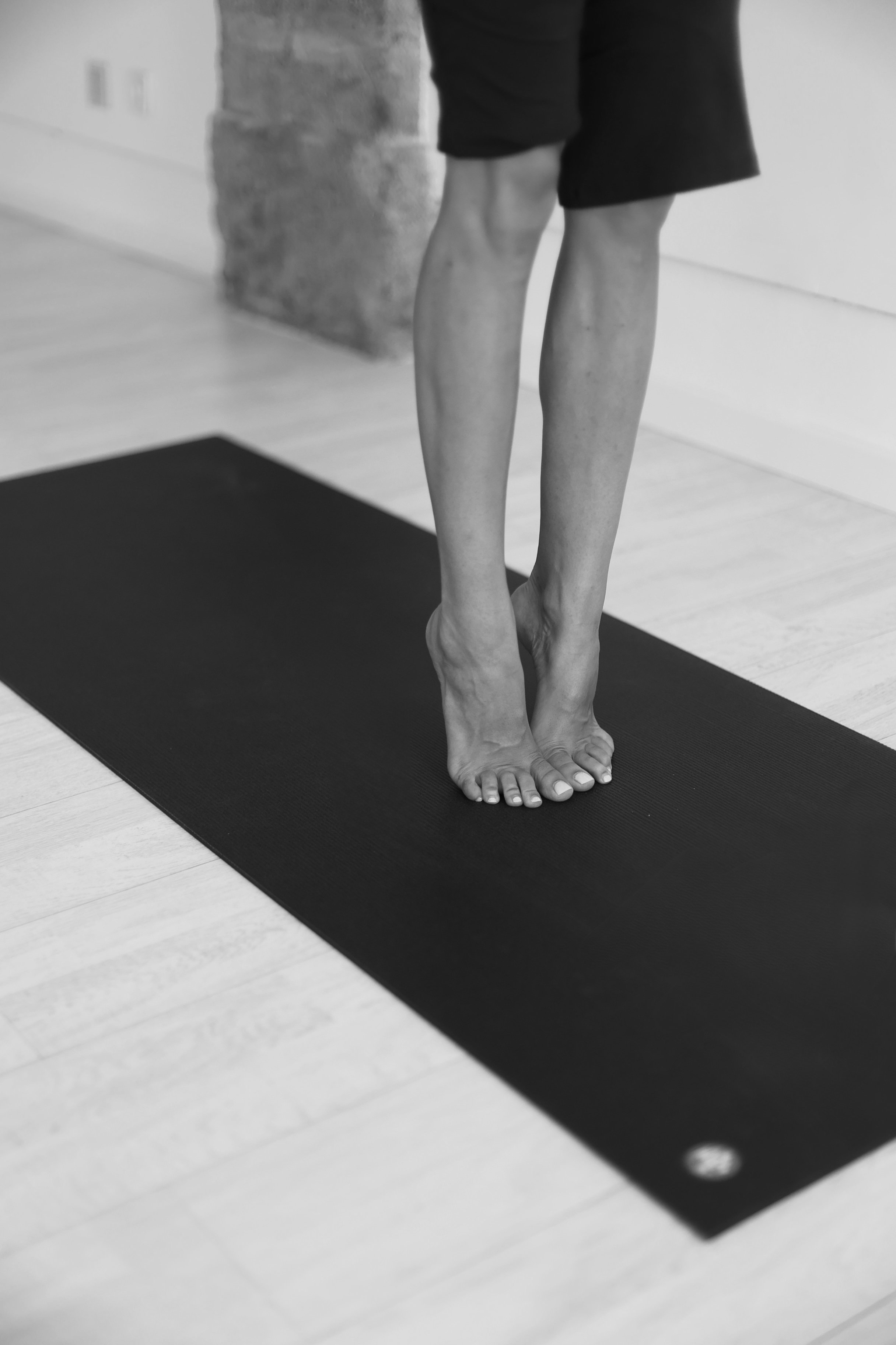 Close-up of a person standing on a yoga mat, preparing for yoga or exercise, with a brick wall and wooden floor in the background.