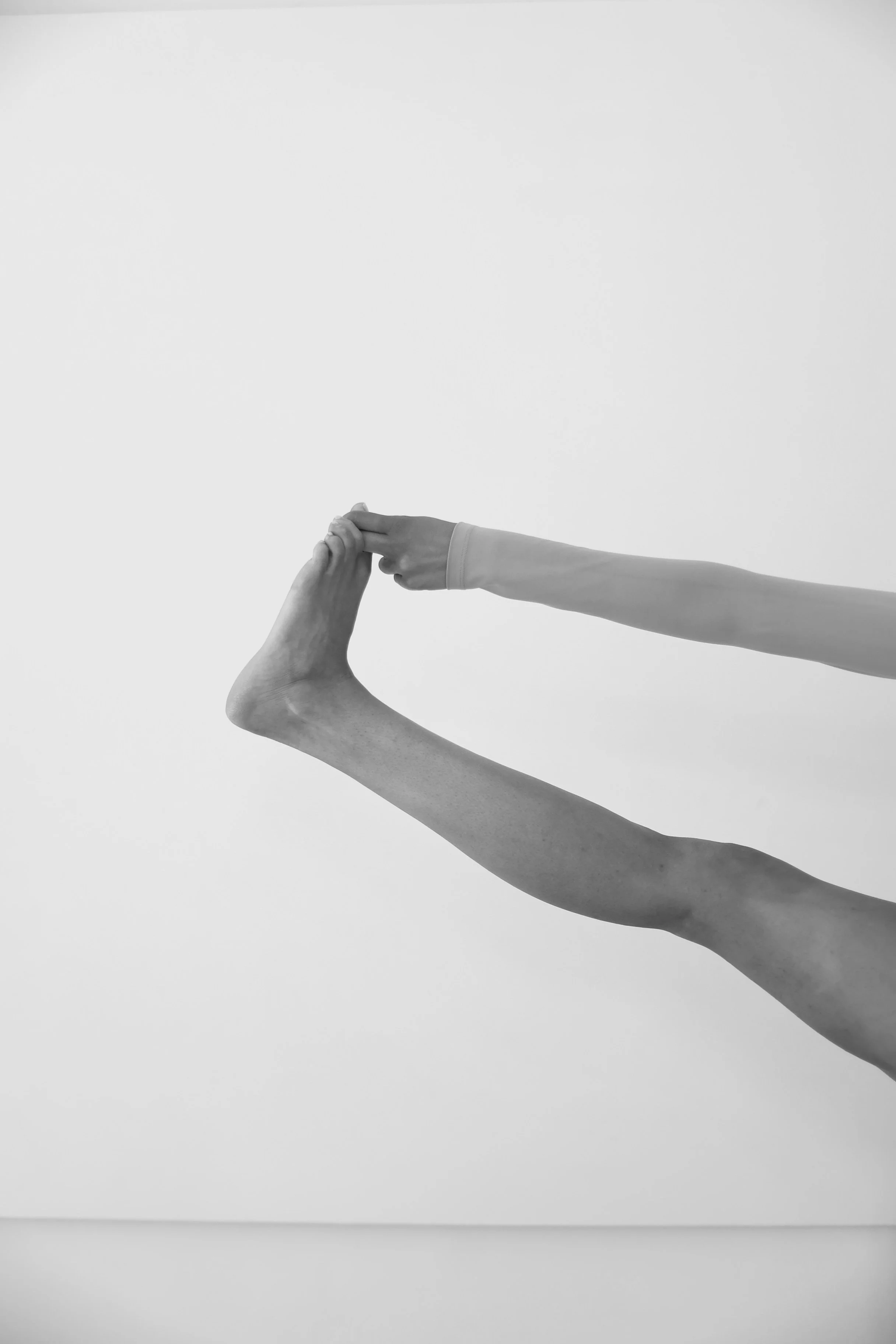 A black and white photograph of two arms reaching out and holding hands, with one arm extending from the right and the other from below, against a plain, light background.