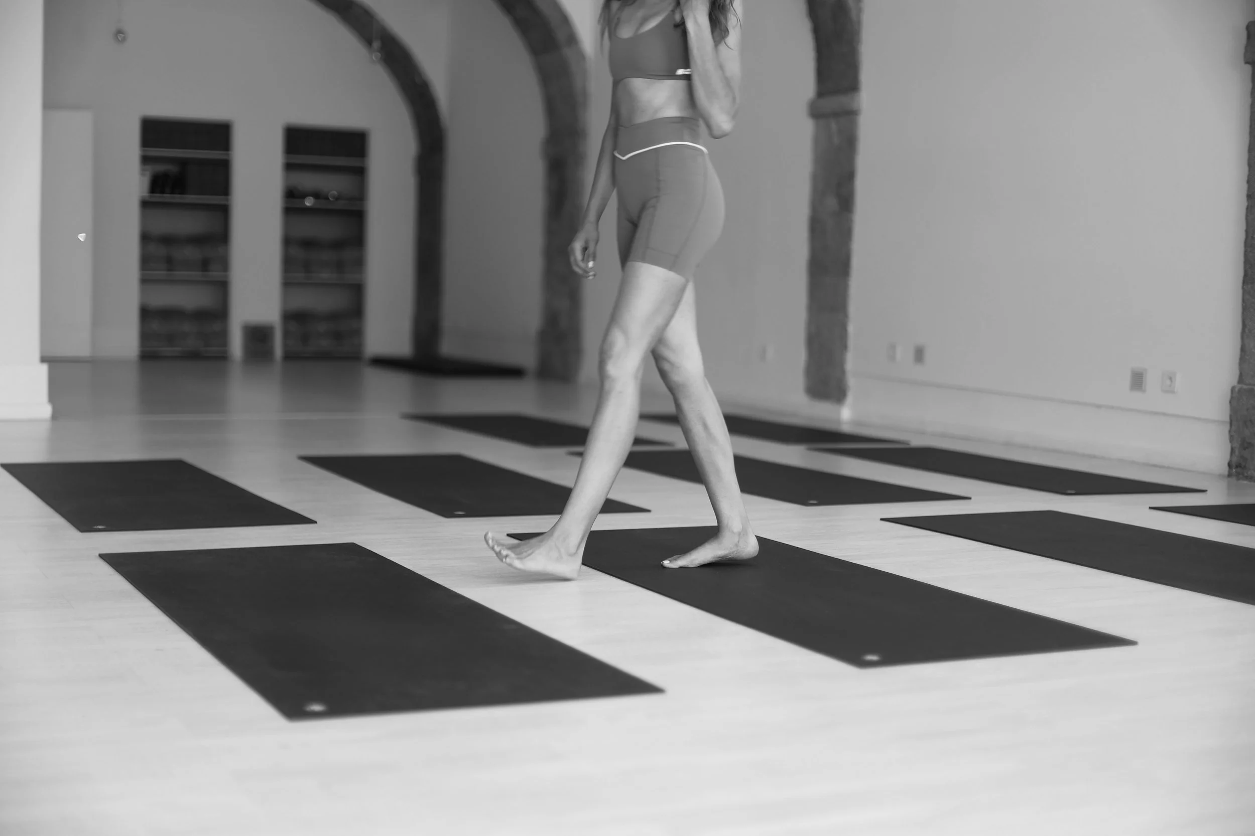 A person practicing yoga on a black mat in a spacious room with stone arches and built-in bookshelves on the wall.
