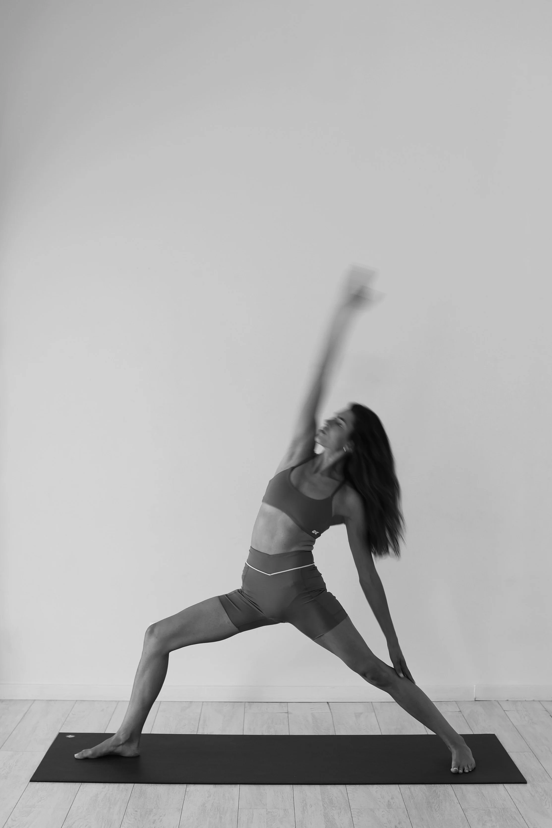 A woman practicing yoga indoors, performing a side plank pose on a yoga mat, wearing athletic wear, with one arm extended upward and her gaze upward.