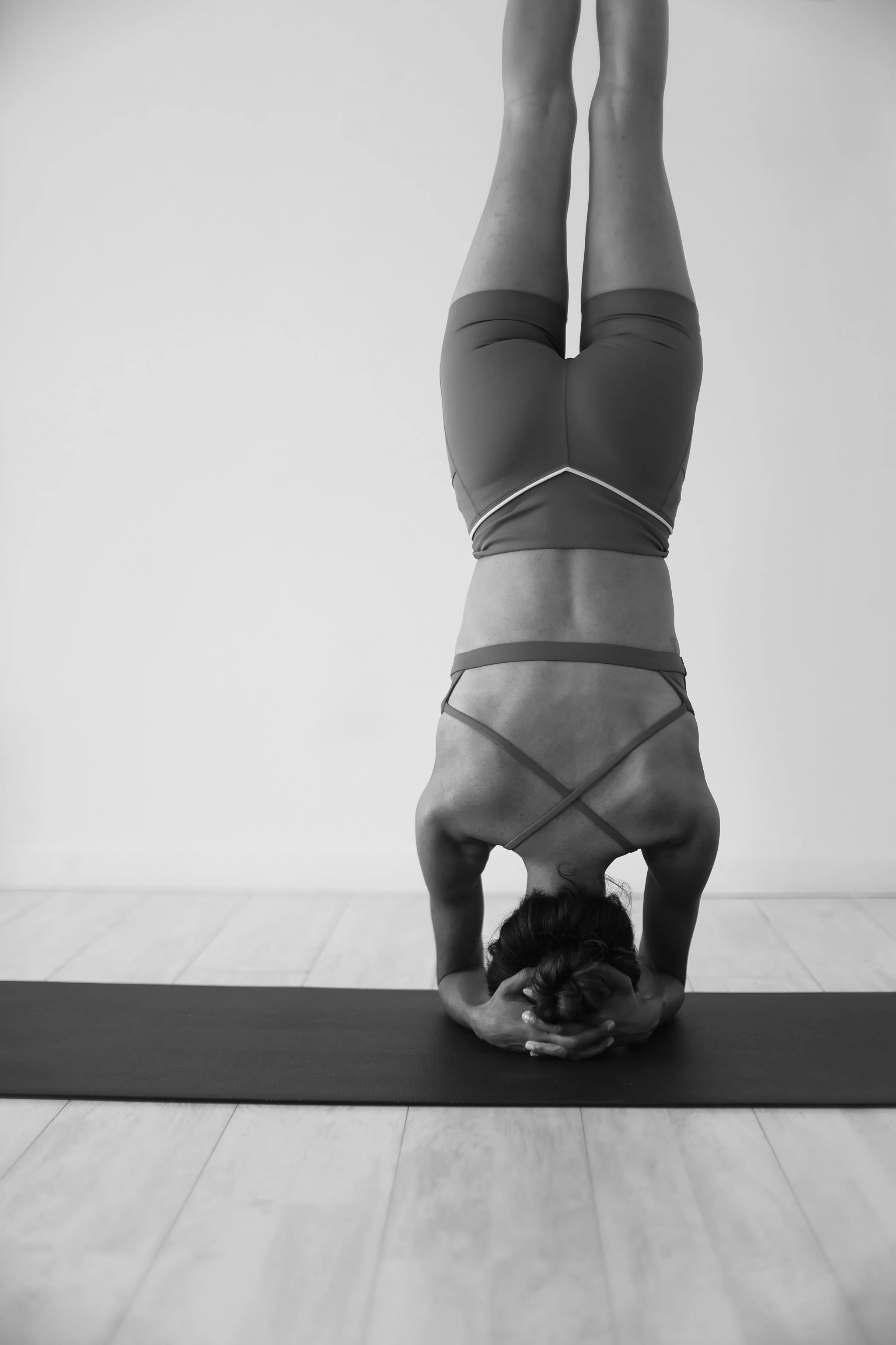 A woman practicing yoga in a headstand pose on a yoga mat indoors, with a plain wall background.