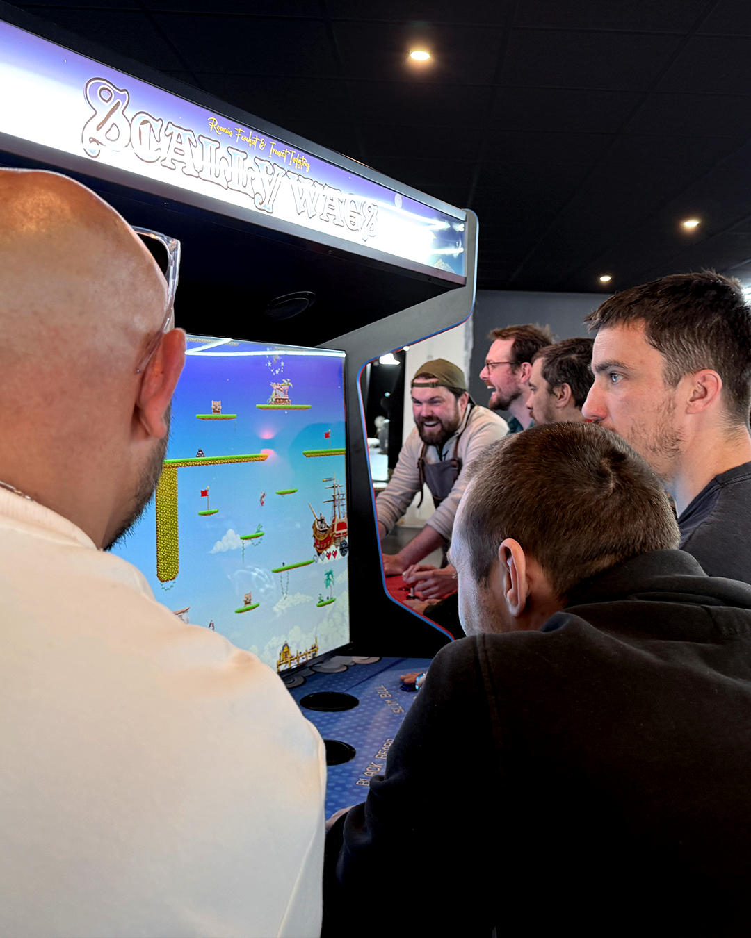 Groupe de personnes jouant à Scallywags arcade dans une salle sombre.