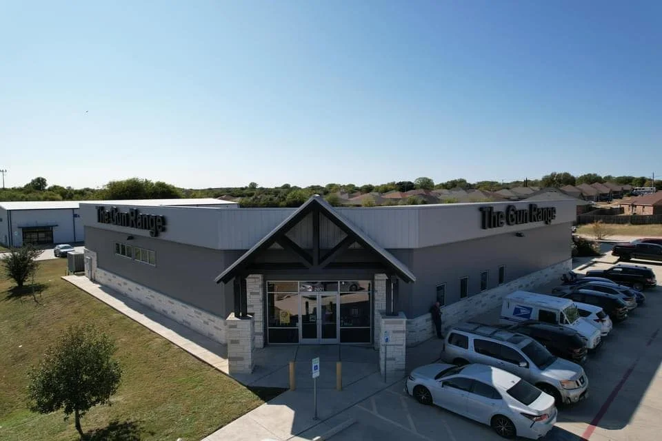 Exterior view of The Gun Range building with parking lot, blue sky, and some trees.