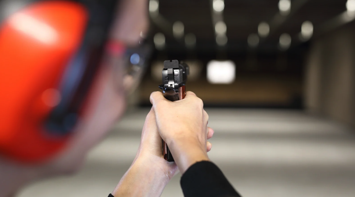 Person aiming a handgun at a shooting range with a blurred target in the background.