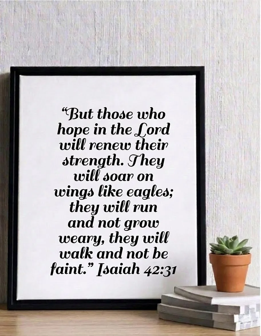 A framed typography print of the Bible verse Isaiah 42:31 displayed on a rustic wooden surface next to a small potted succulent and a stack of books