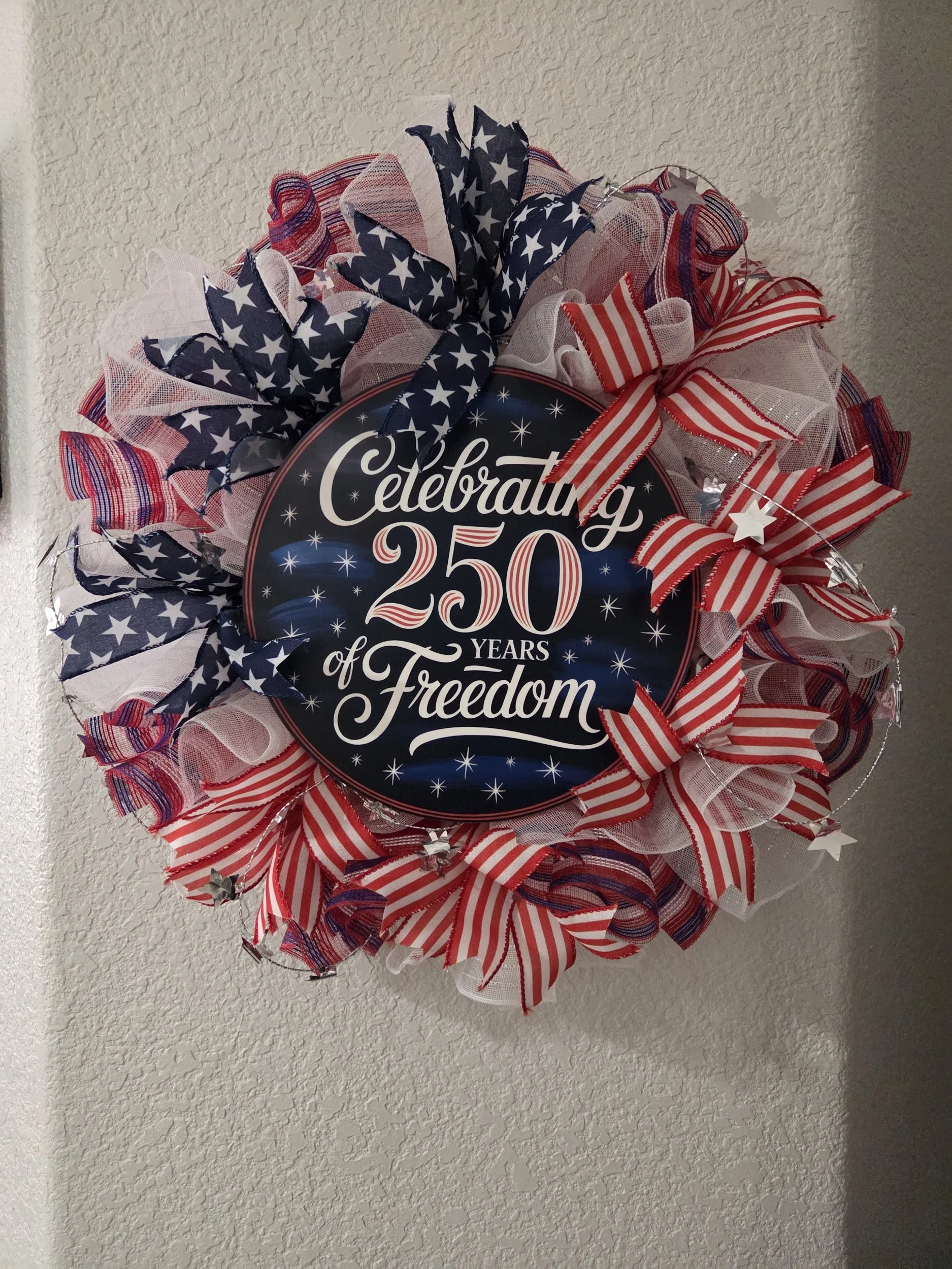 A patriotic wreath with red, white, and blue ribbons and a sign celebrating 250 years of freedom.