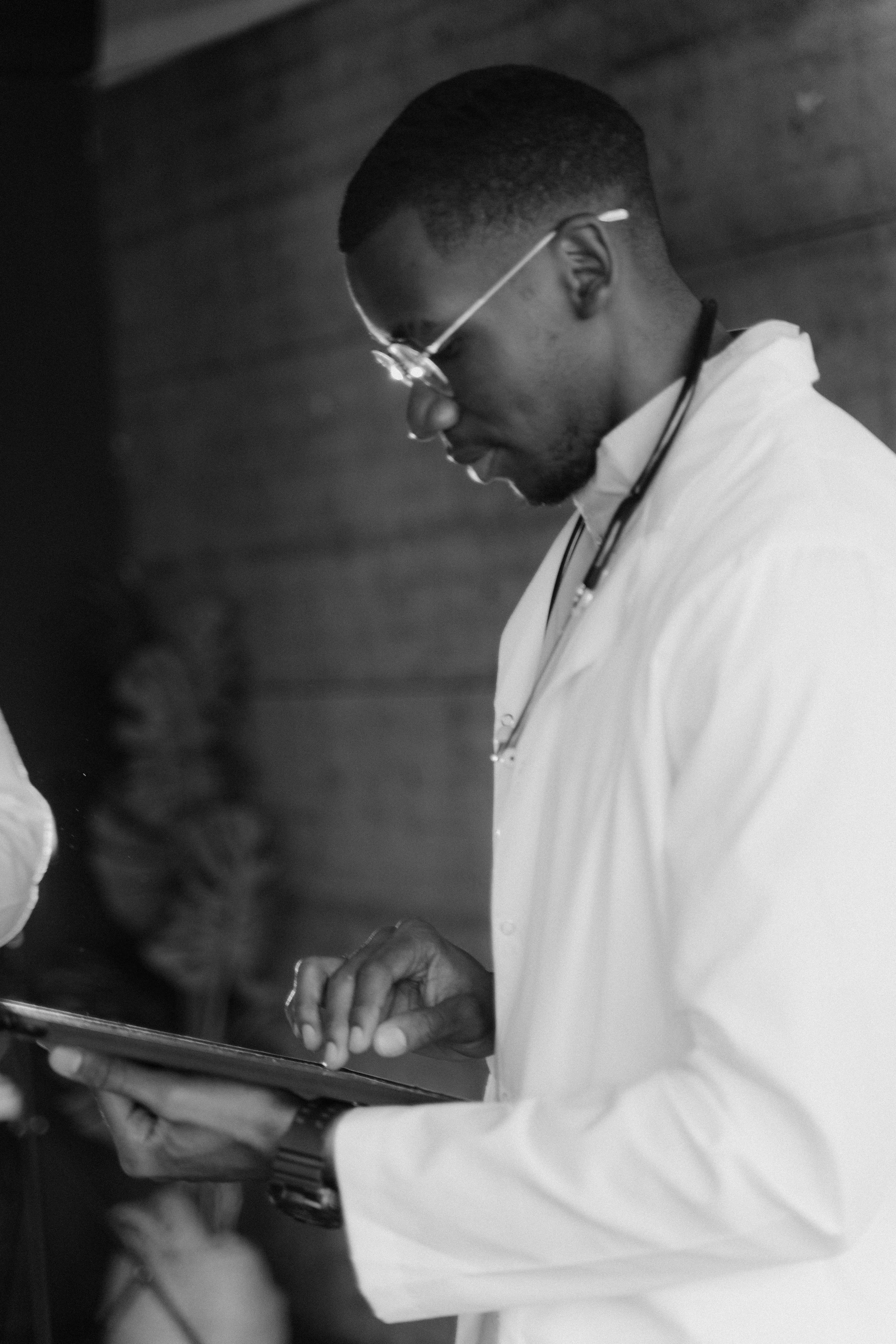 A man wearing glasses and a white shirt using a stethoscope. He appears to be examining or listening to a patient or a document.