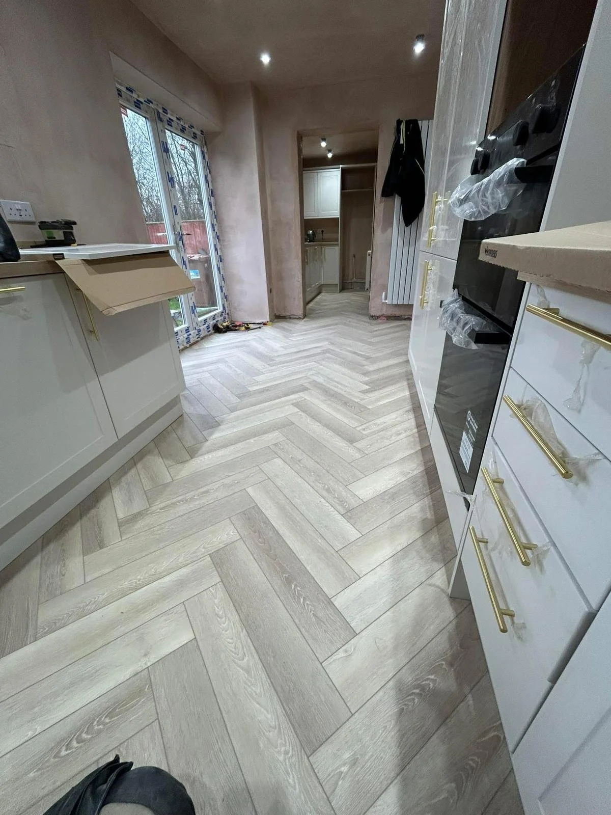 A kitchen under renovation with incomplete walls, new flooring, and partially installed cabinets and appliances.