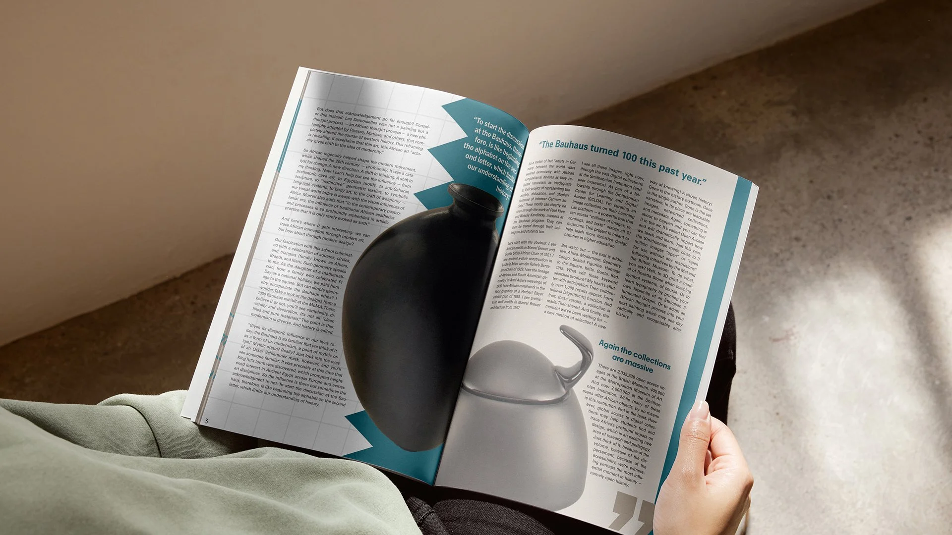 A person sitting and reading a magazine, holding it with one hand. The magazine features images of a black vase with a curved handle, a white sculpture, and text discussing art, the Bauhaus movement, and the 100th anniversary.