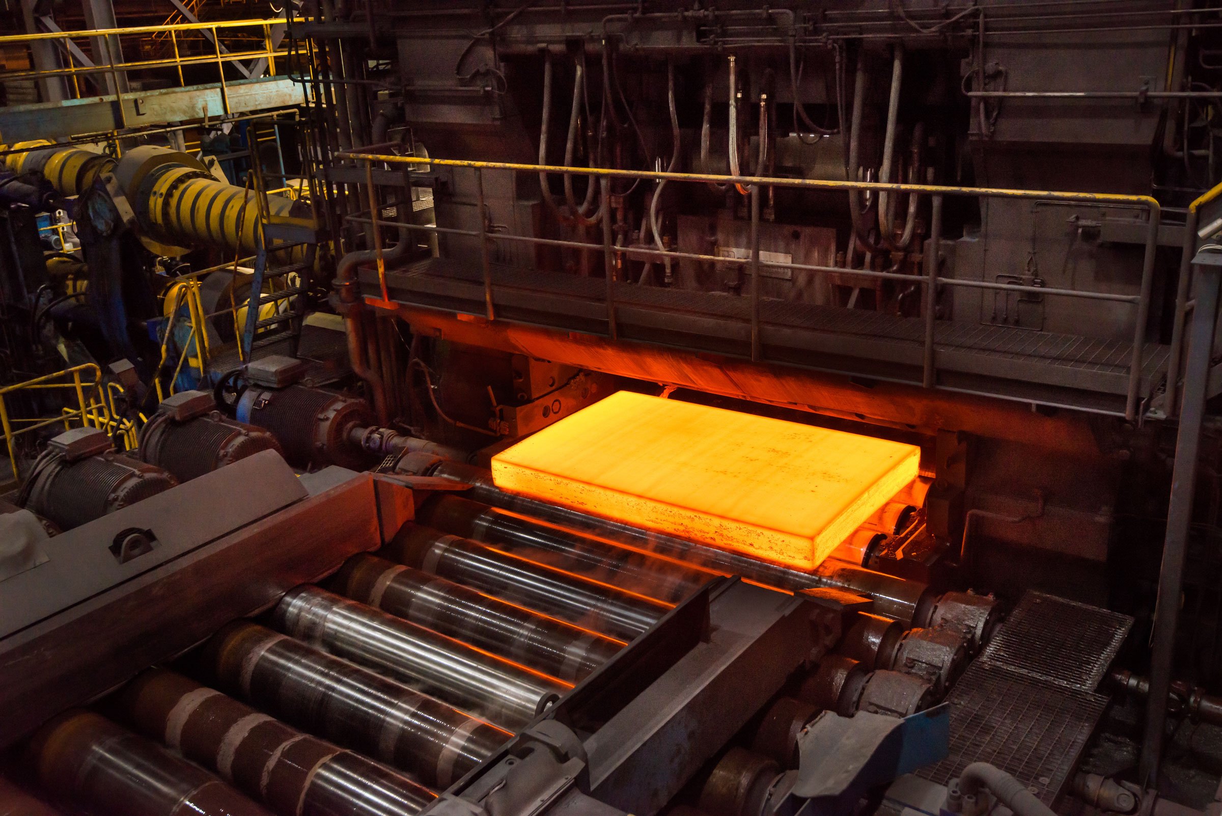 Industrial manufacturing equipment with heated rollers and glowing orange metal sheet