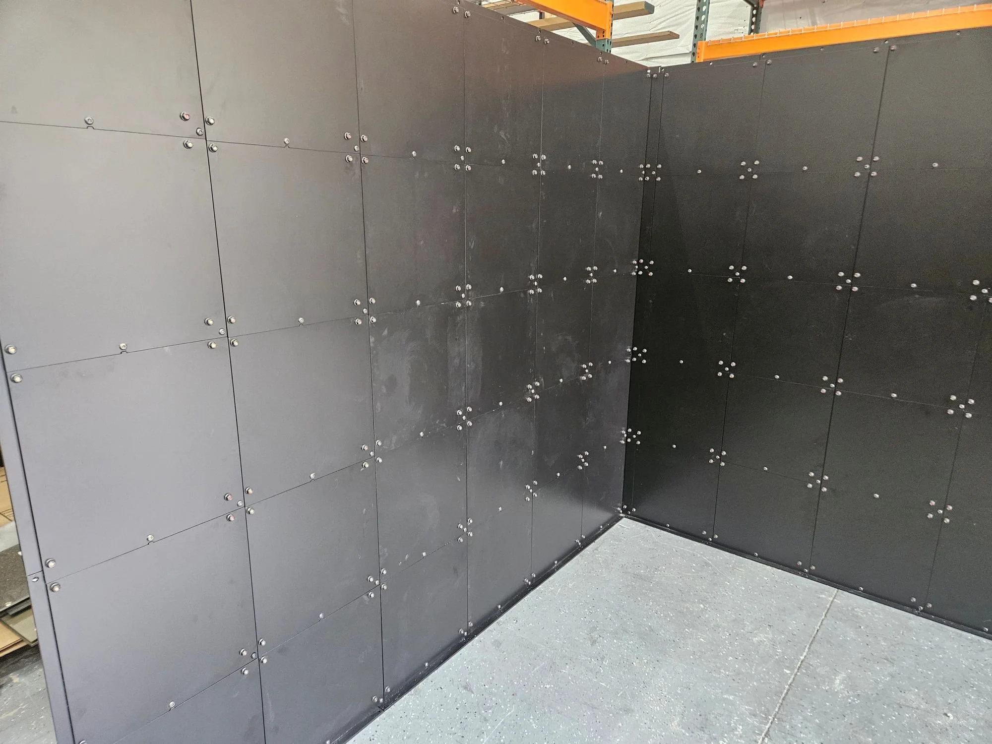 Black storage or industrial cabinets with metal bolts, in a warehouse or industrial setting.