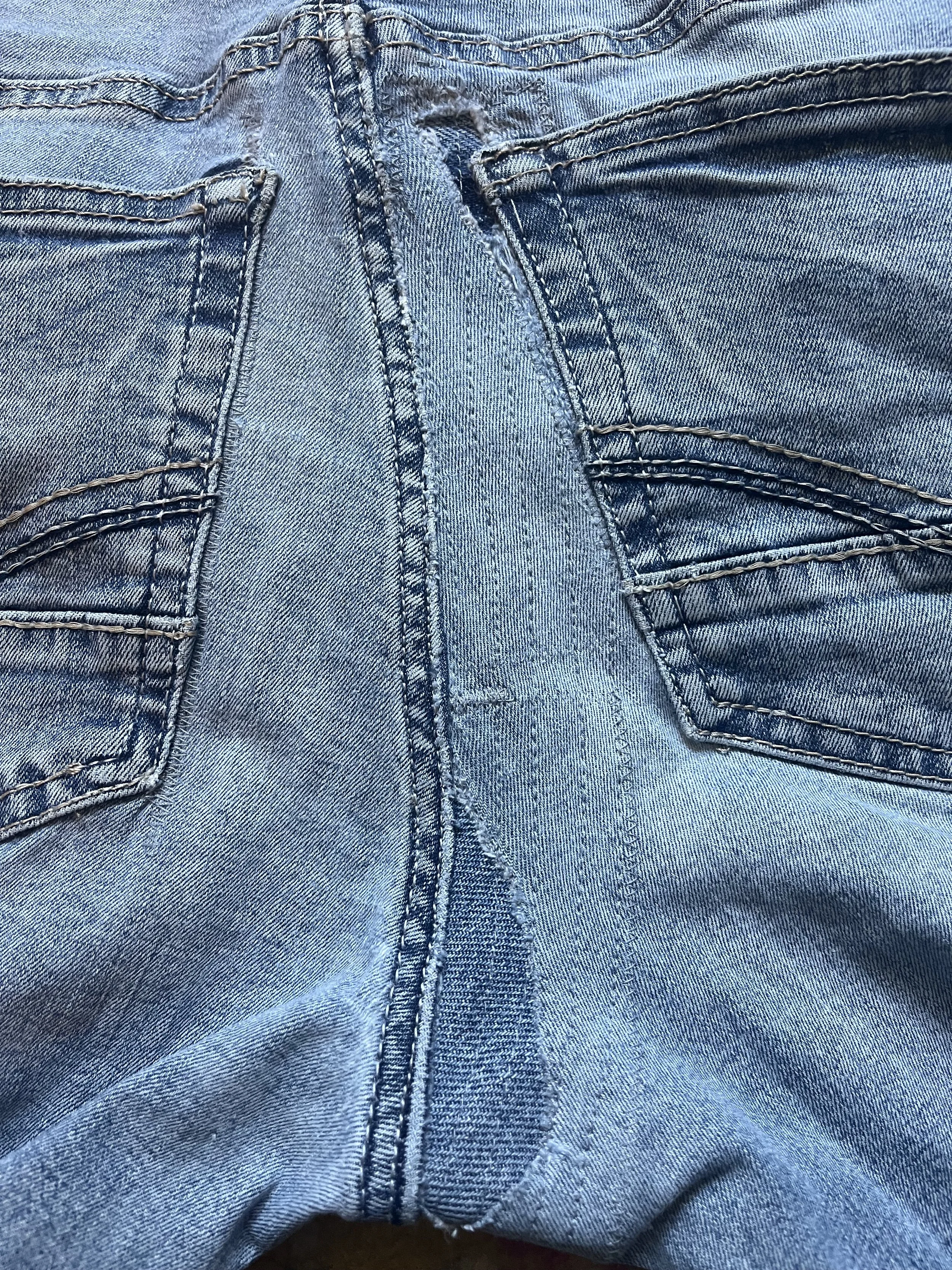 Close-up view of the crotch and upper thigh area of blue denim jeans showing the zipper and stitched pockets.