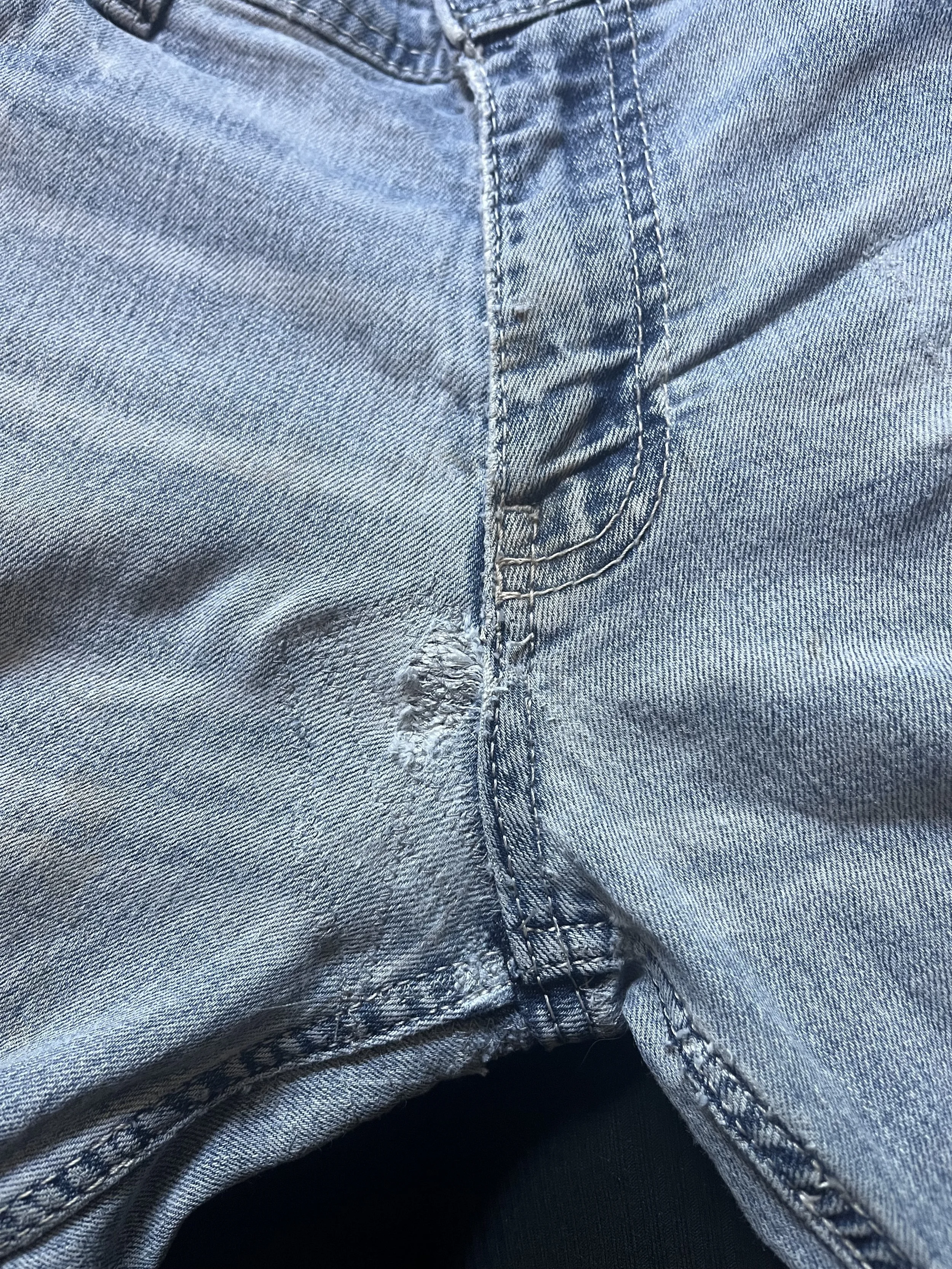 Close-up of a pair of light blue denim jeans with a front zipper and visible stitching.