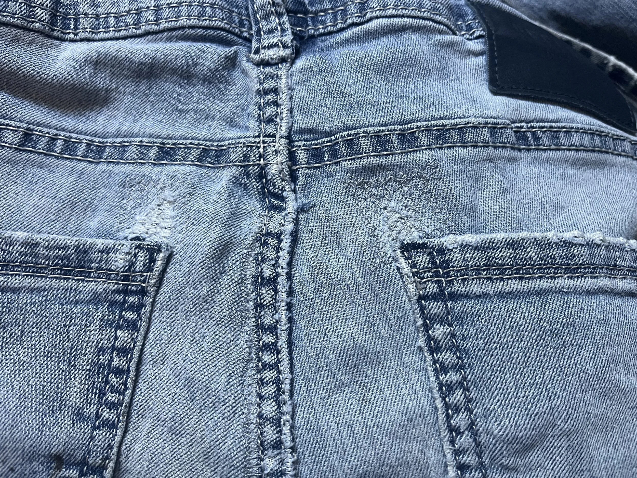 Close-up of blue denim jeans showing stitching, waistband, and partial pocket.