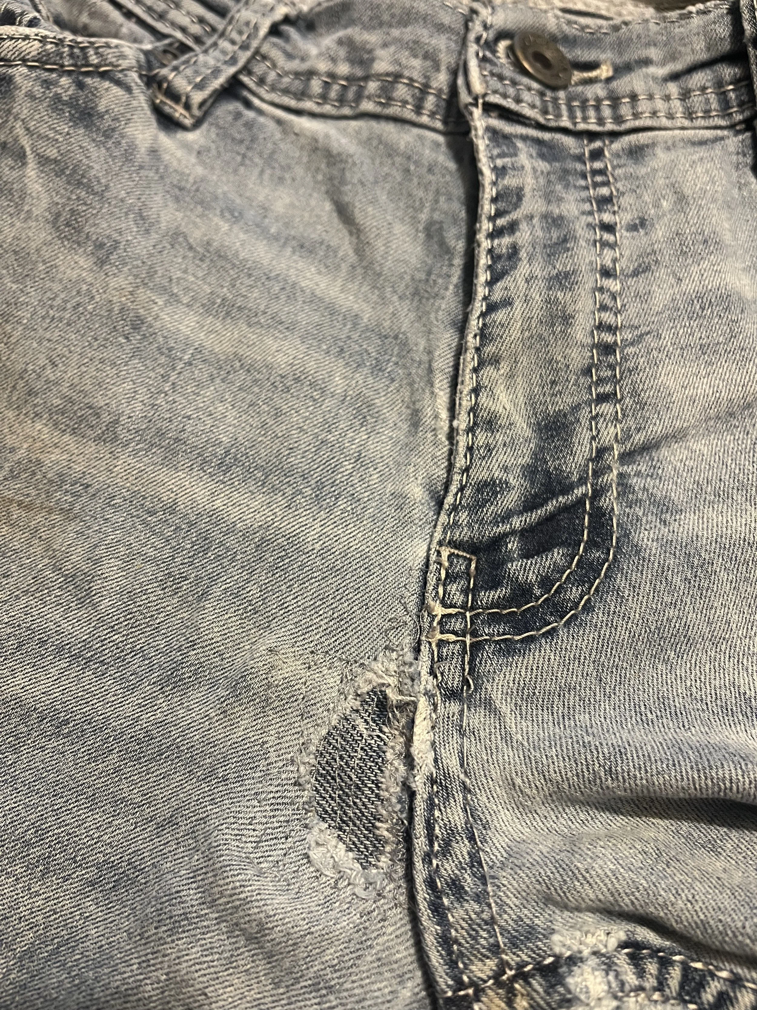 Close-up of worn light gray denim jeans with visible stitching, a button, and distressed fabric near the crotch area.