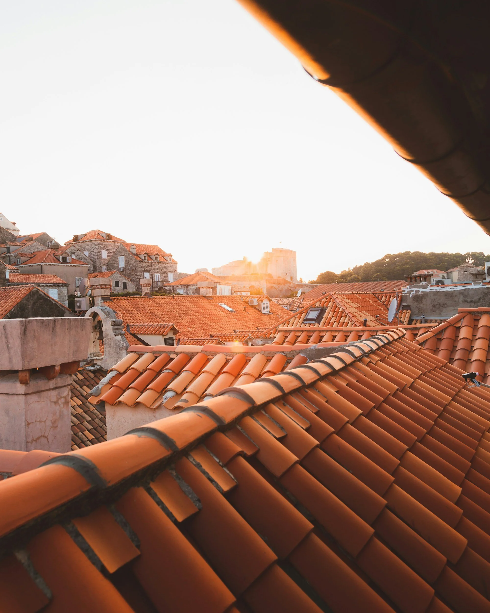Toit avec tuiles en terre cuite orange dans une vieille ville avec des bâtiments en pierre et des cheminées, au coucher du soleil.