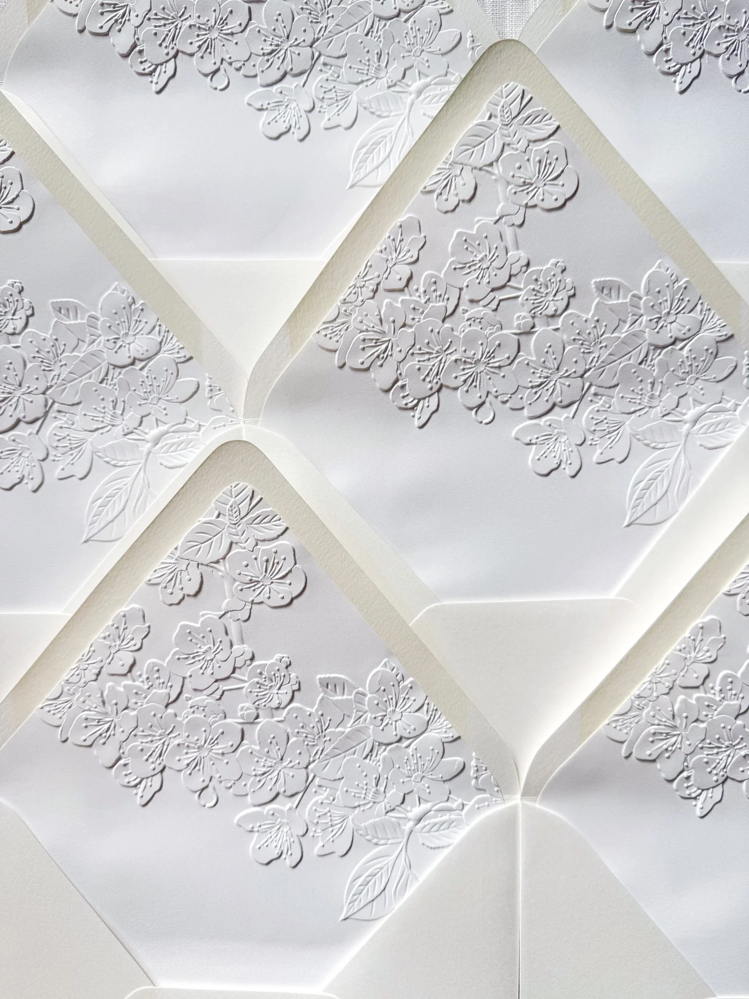 White embossed envelope liners with floral designs and leaves, layered in an intricate pattern.