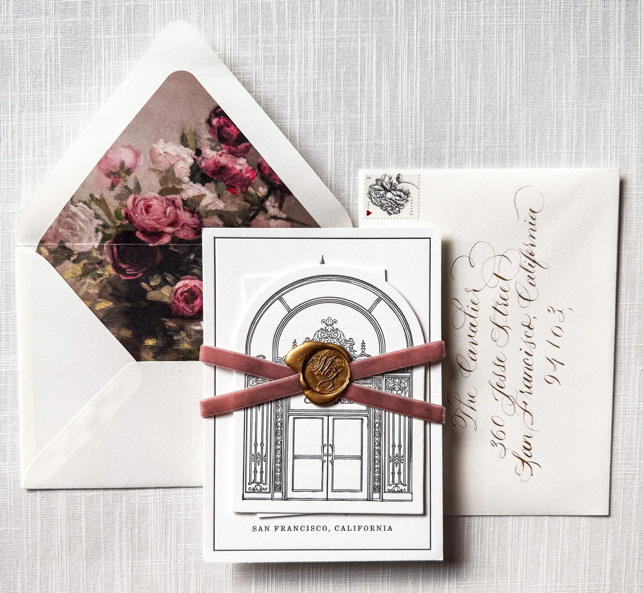 A collection of stationery and cards including an envelope with a floral interior, a postmarked card with a wax seal, and handwritten script, all arranged on a textured surface, with a focus on elegant design and decorative details.