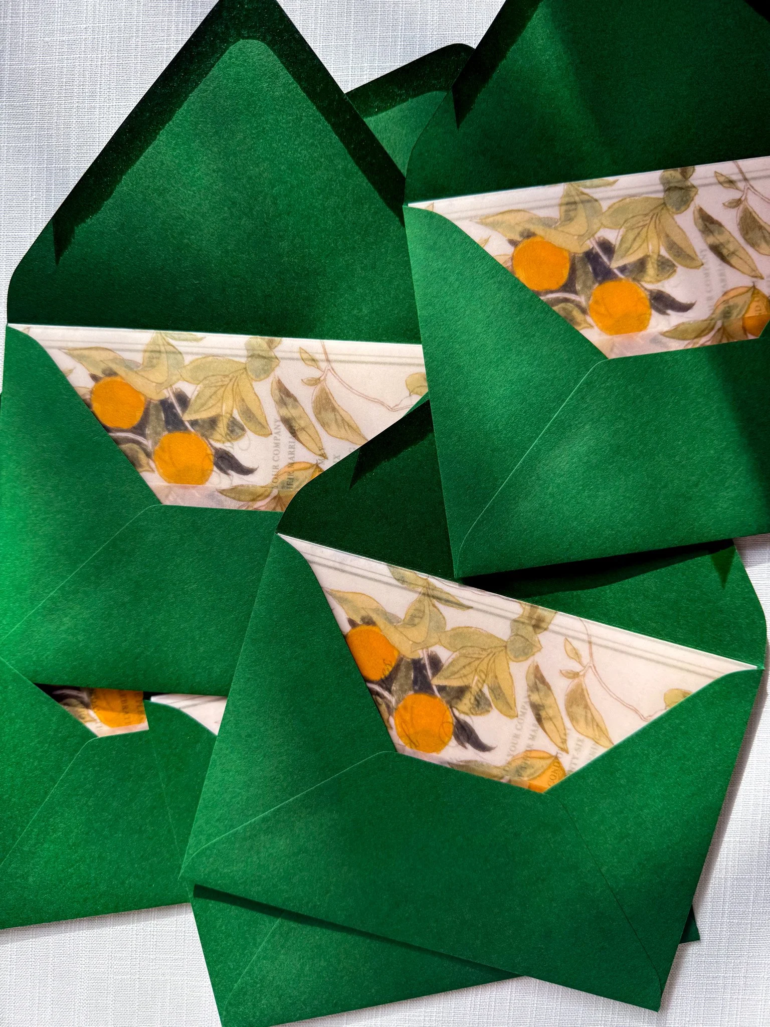 A vellum wrap featuring a pattern of orange fruits and leaves, placed in green envelopes.