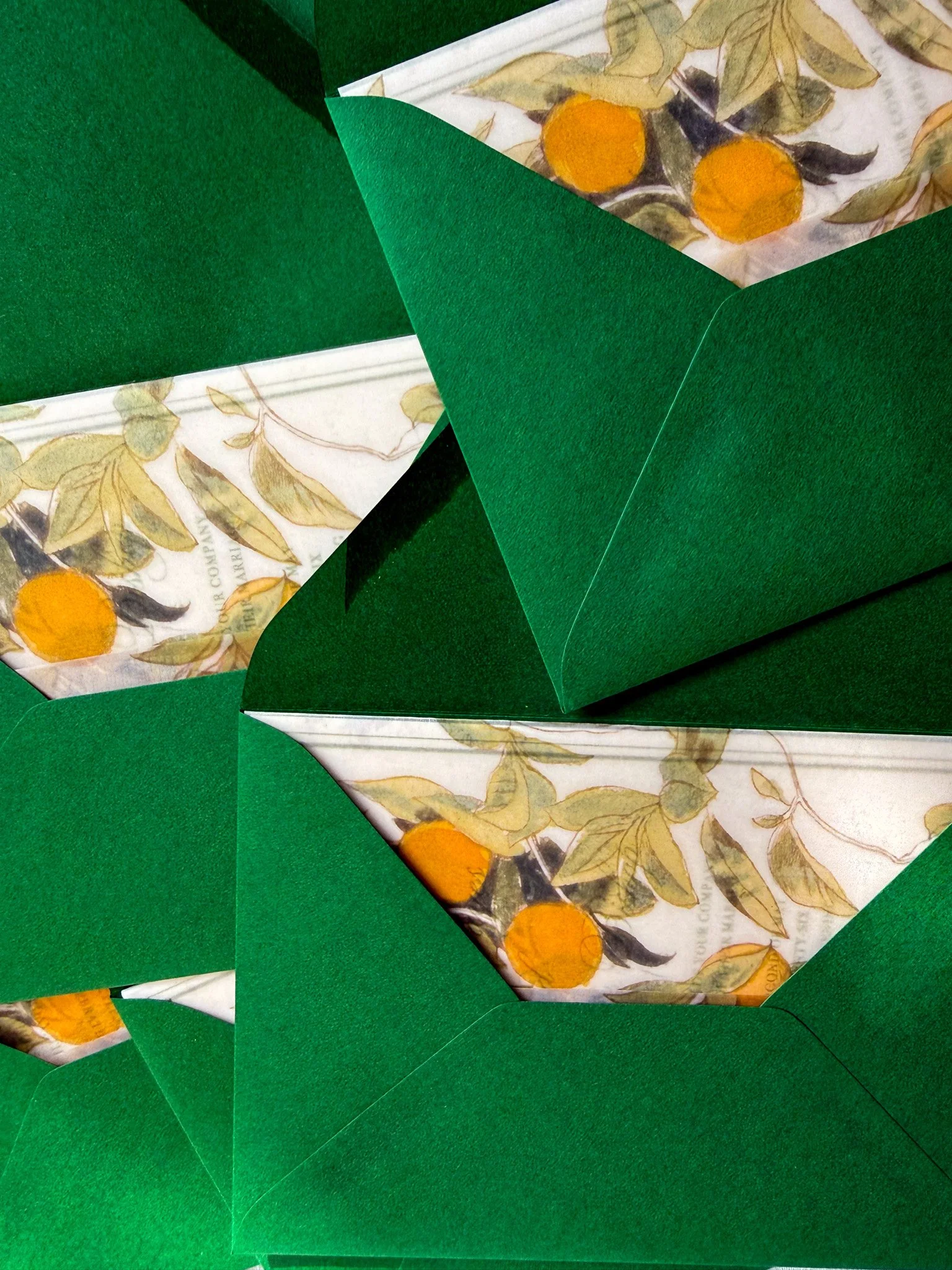 A vellum wrap featuring a pattern of orange fruits and leaves, placed in green envelopes.