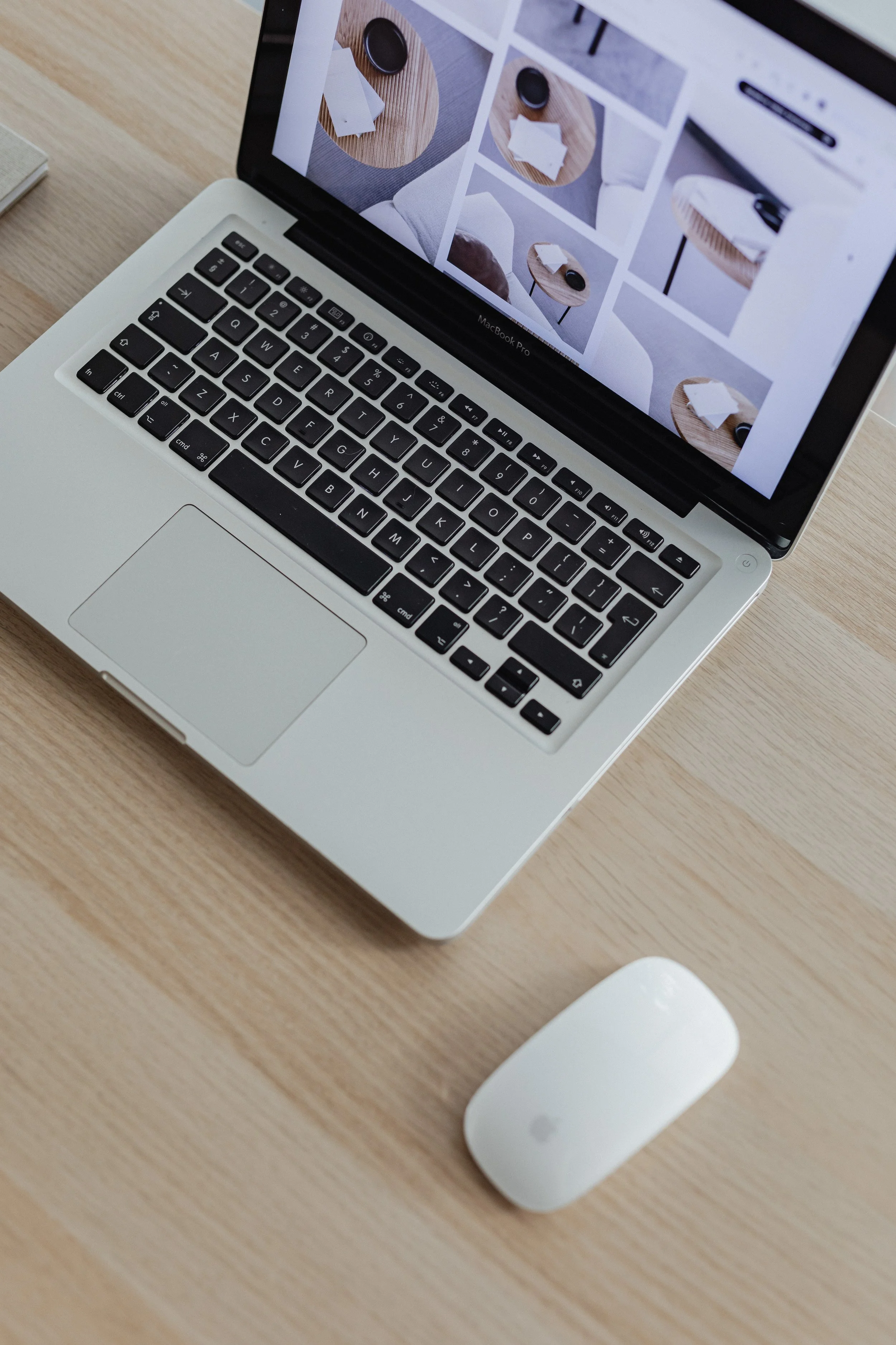 A MacBook Pro laptop on a wooden desk displaying a grid of images featuring coffee cups and wooden tables, with a white Apple Magic Mouse in front of it.