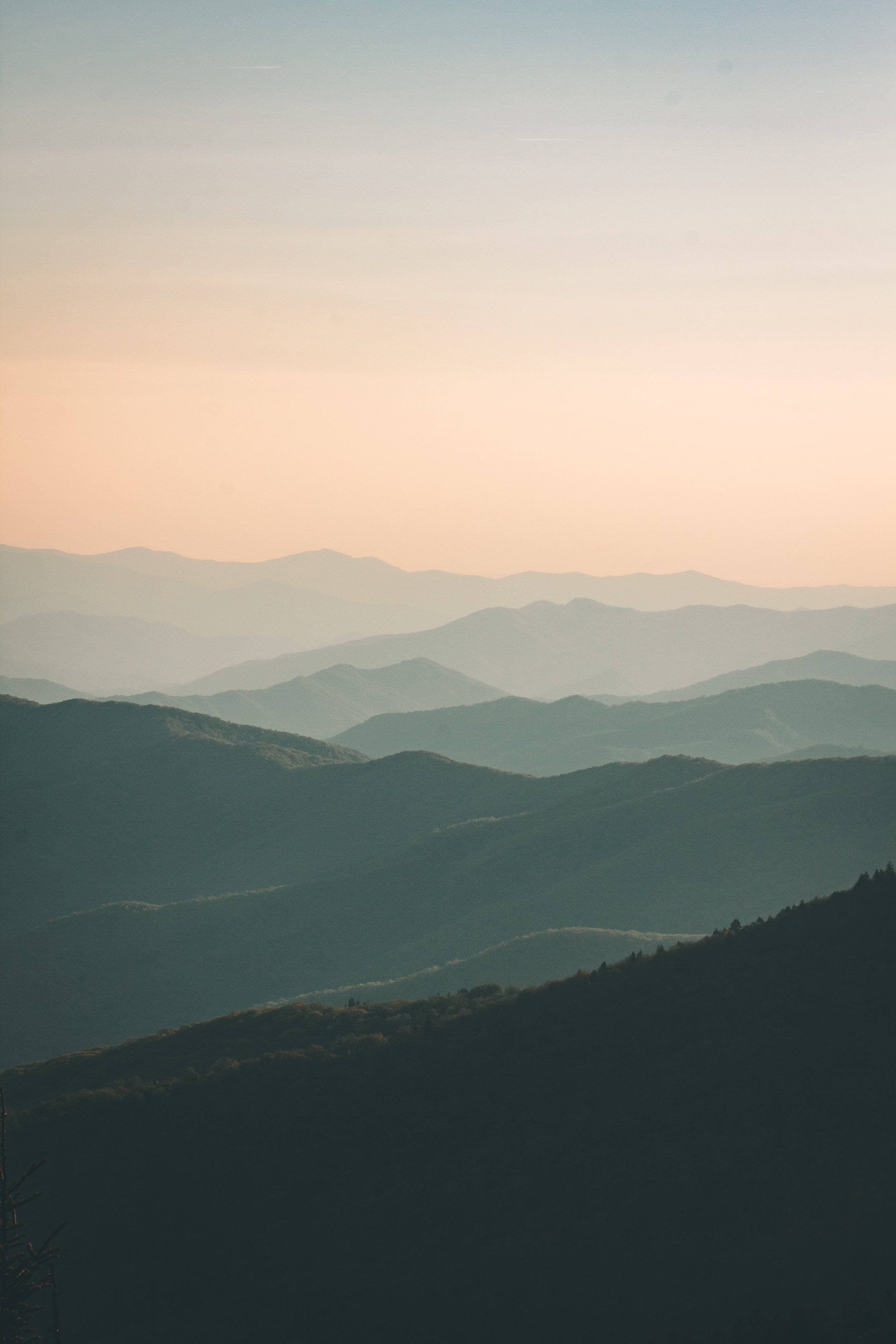 A view of multiple mountain ridges during sunset with a soft gradient sky.